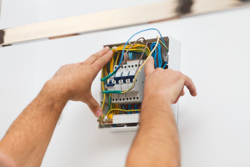 Hands Working on Open Electrical Panel With Colored Wires on a White Wall — CDT Electrical in Lennox Head, NSW
