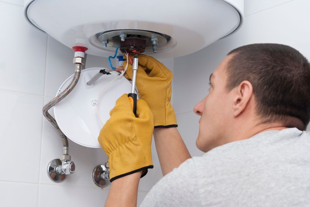 Person in Yellow Gloves Repairs a Hot Water Heater, Working Inside a White Bathroom — CDT Electrical in Lennox Head, NSW