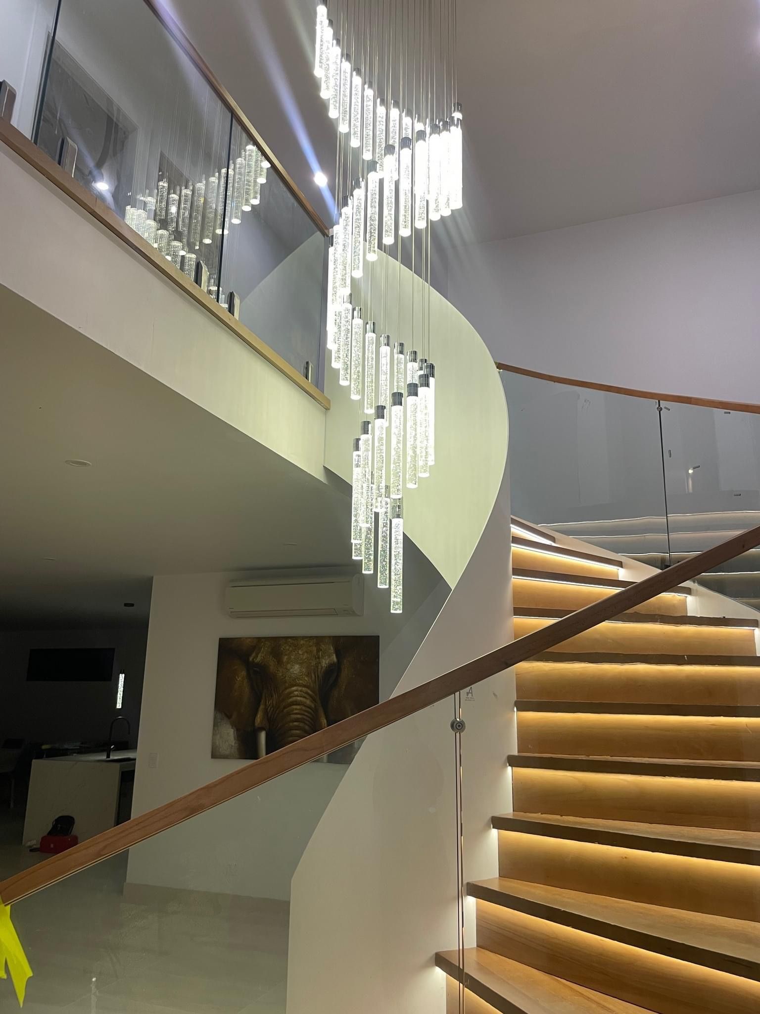 Spiral staircase with wood steps, glass railing, and modern chandelier— CDT Electrical in Lennox Head, NSW