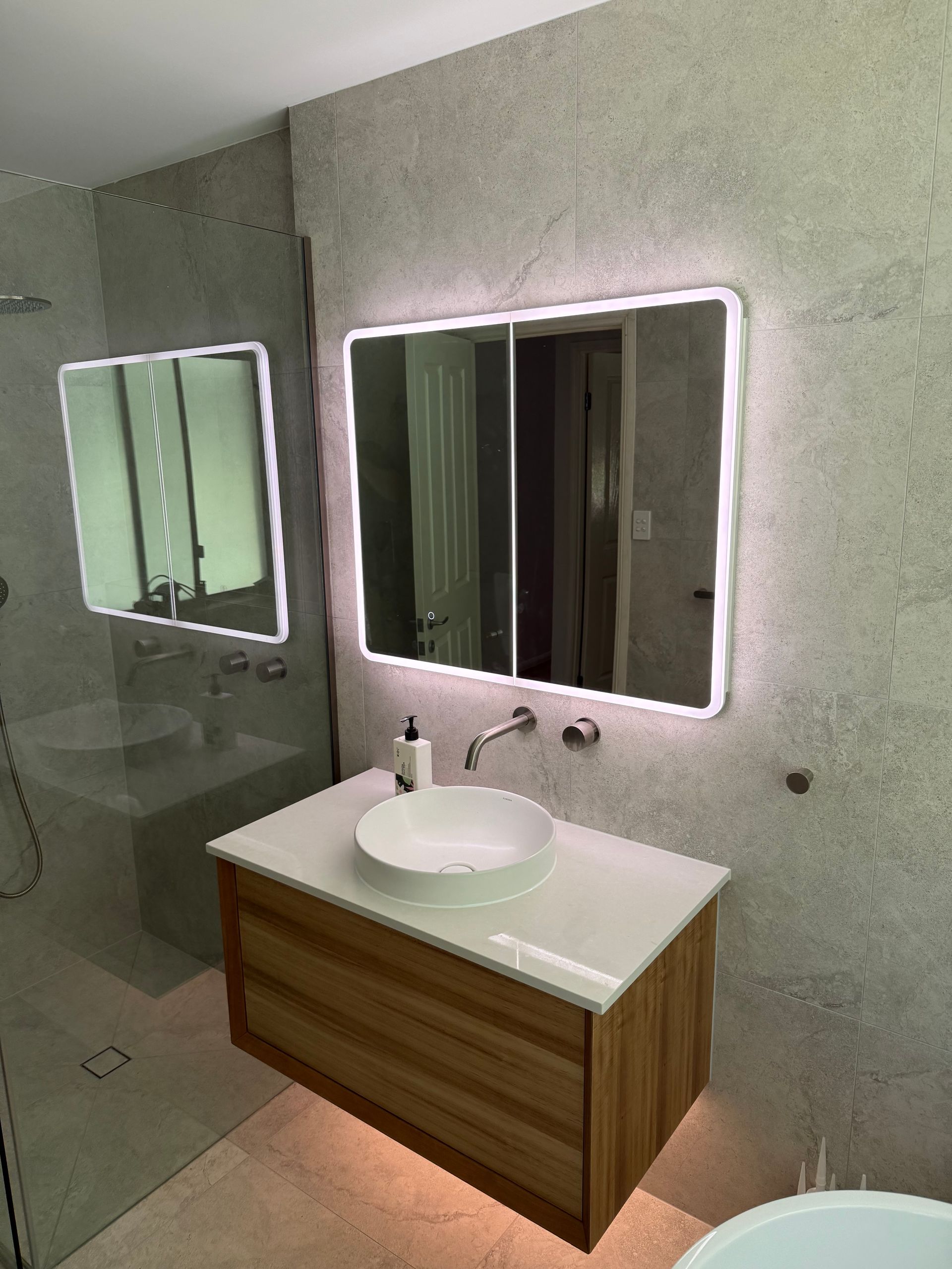 Modern Bathroom With Wood Vanity, White Countertop, Round Sink, and Backlit Mirrors — CDT Electrical in Lennox Head, NSW