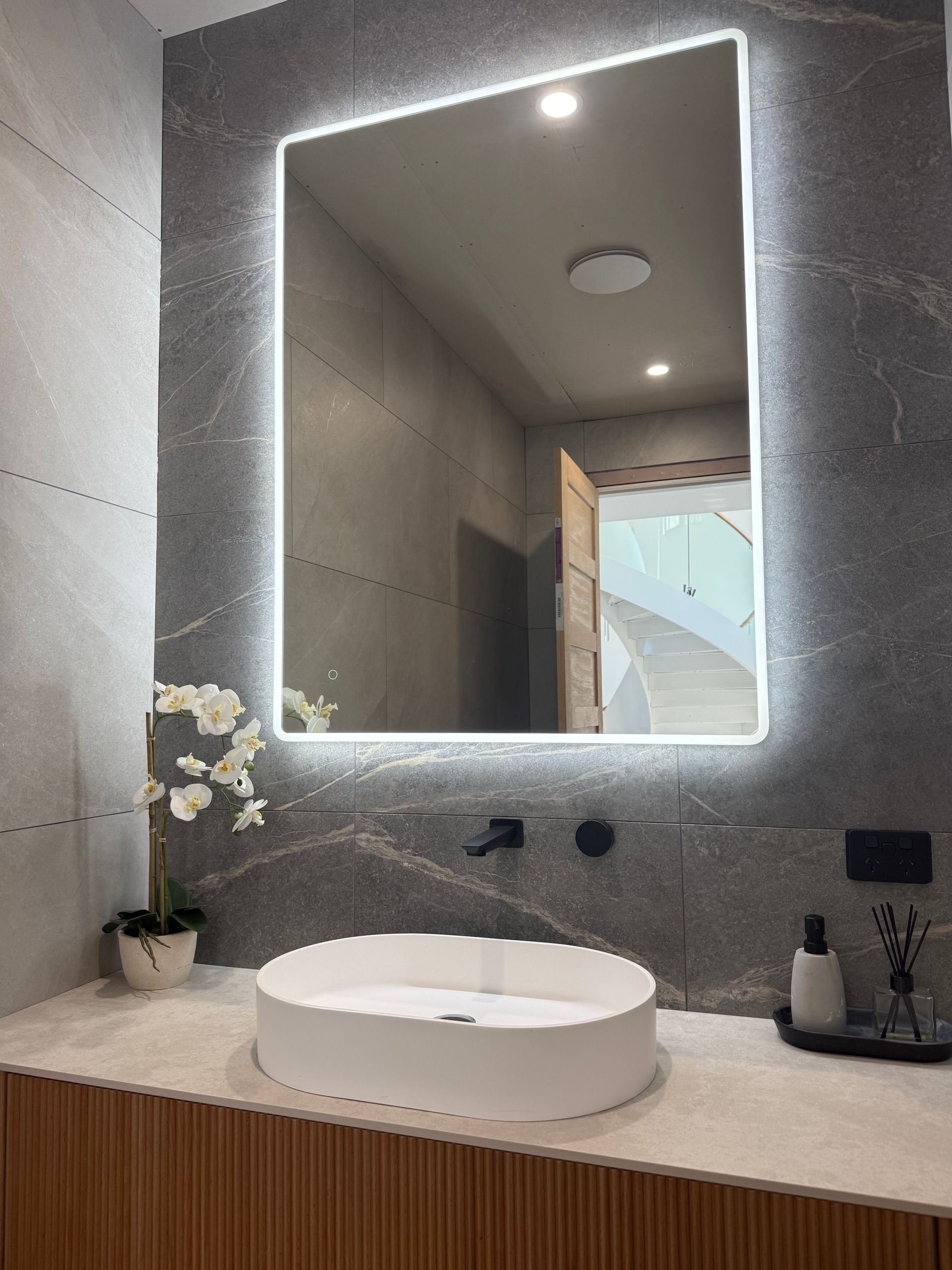 Modern Bathroom With a Glowing-edged Mirror Above a White, Oval Basin — CDT Electrical in Lennox Head, NSW