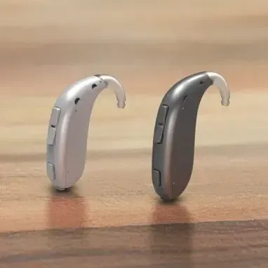 Two hearing aids are sitting on a wooden table.