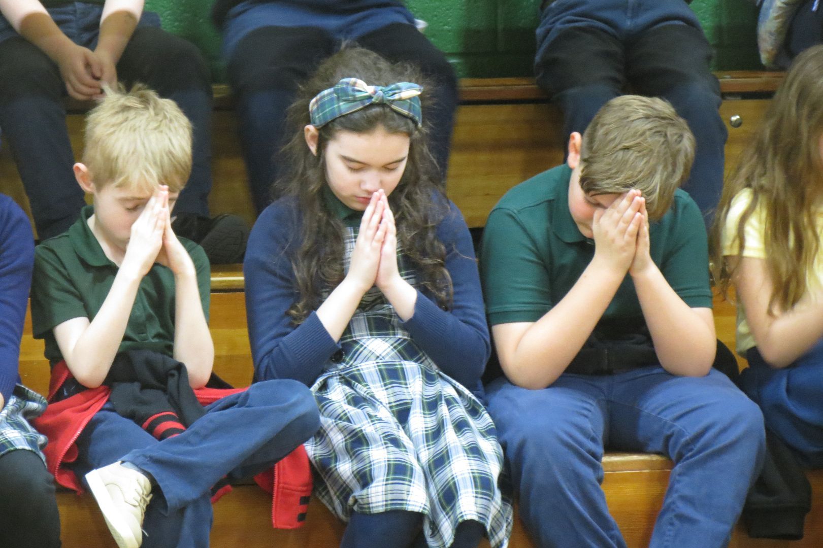 A group of children are sitting on the bleachers with their hands folded in prayer
