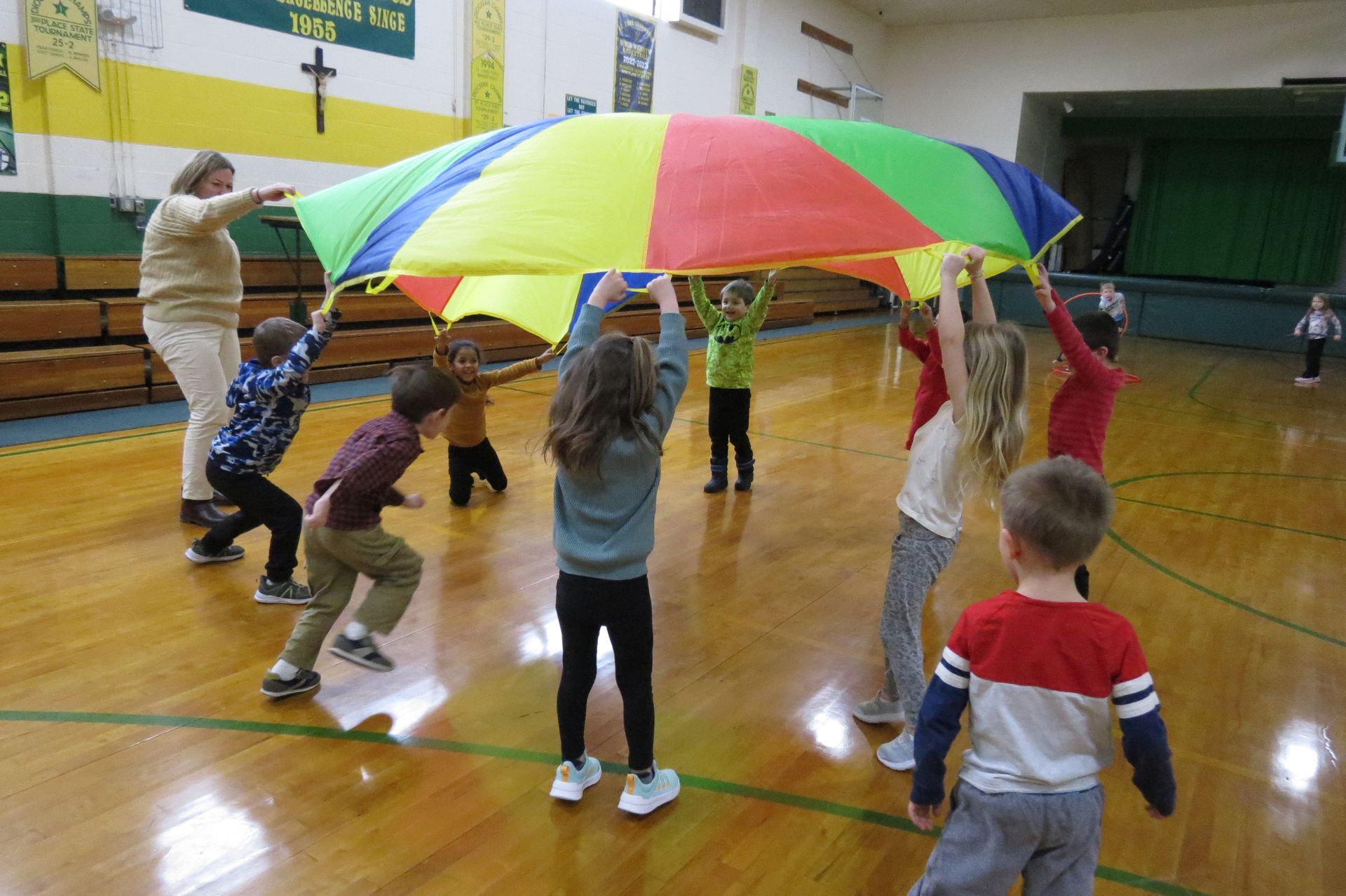 A group of children are playing with a colorful parachute in a gym