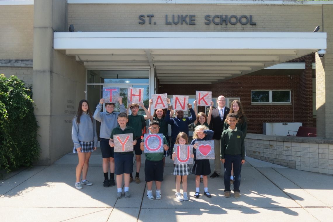 A group of children holding up thank you signs in front of st. luke school