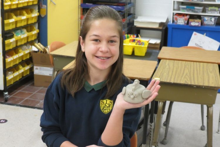A girl in a school uniform is holding a piece of clay