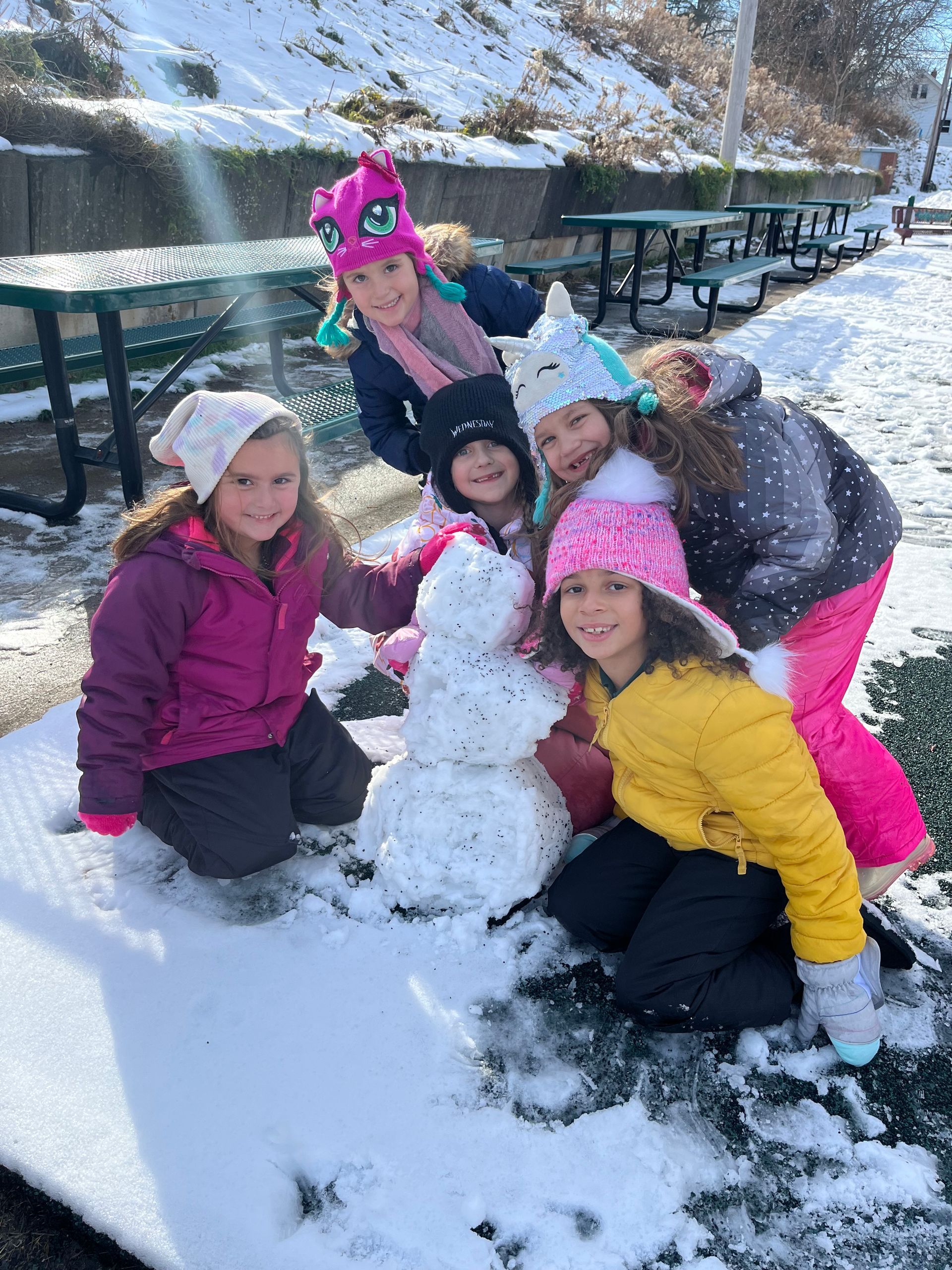 A group of young girls are kneeling around a snowman