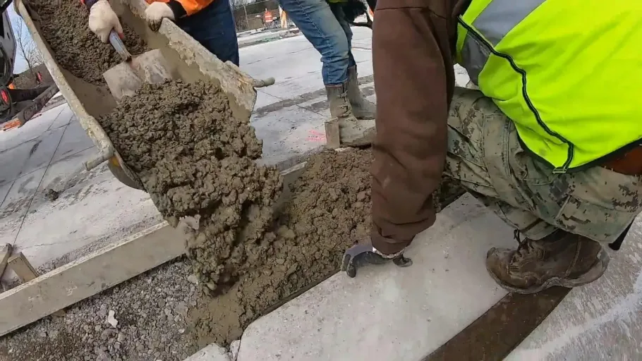 Worker pouring concrete into a wooden curb form.