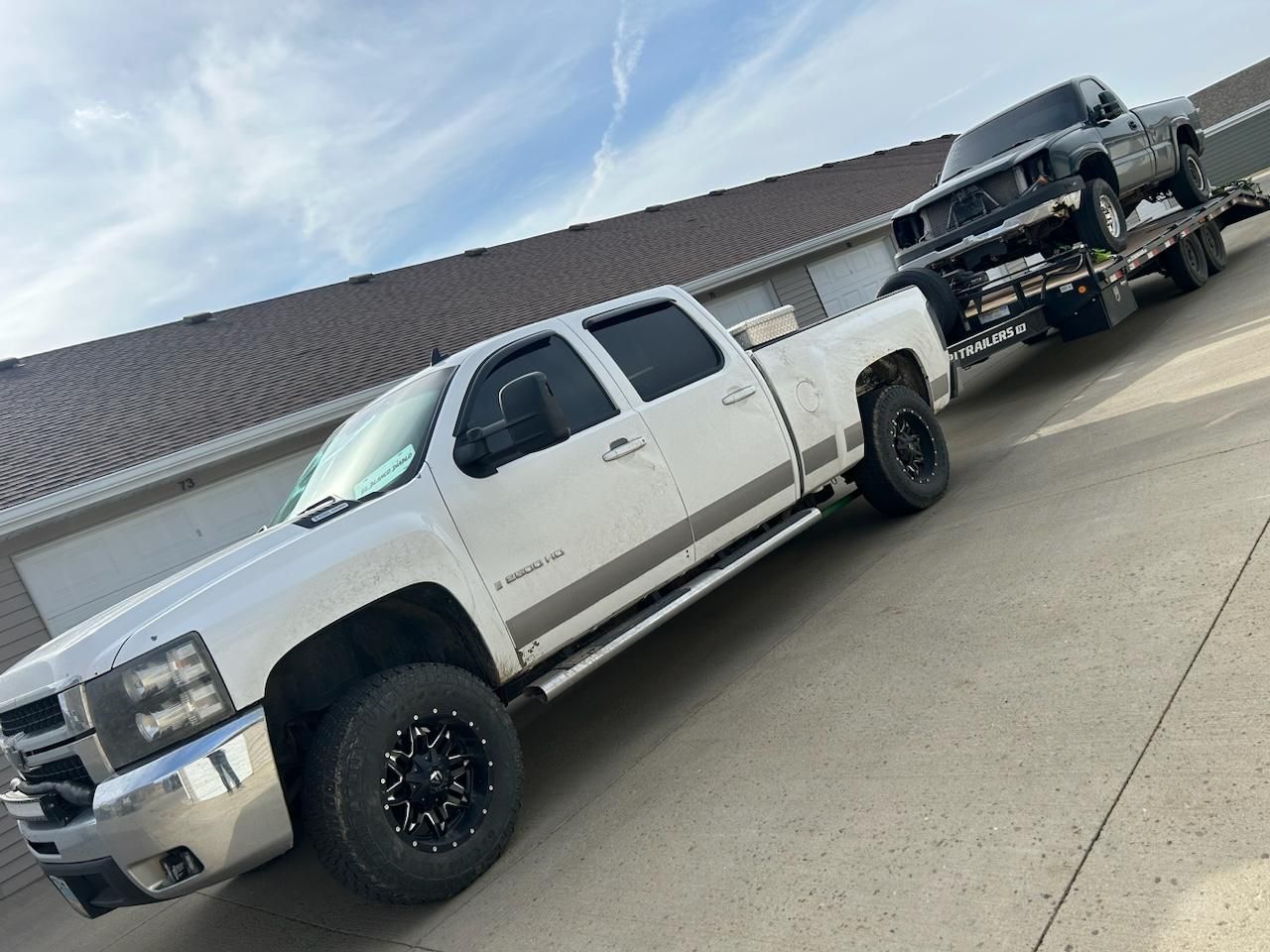A white truck is towing a black truck on a trailer.