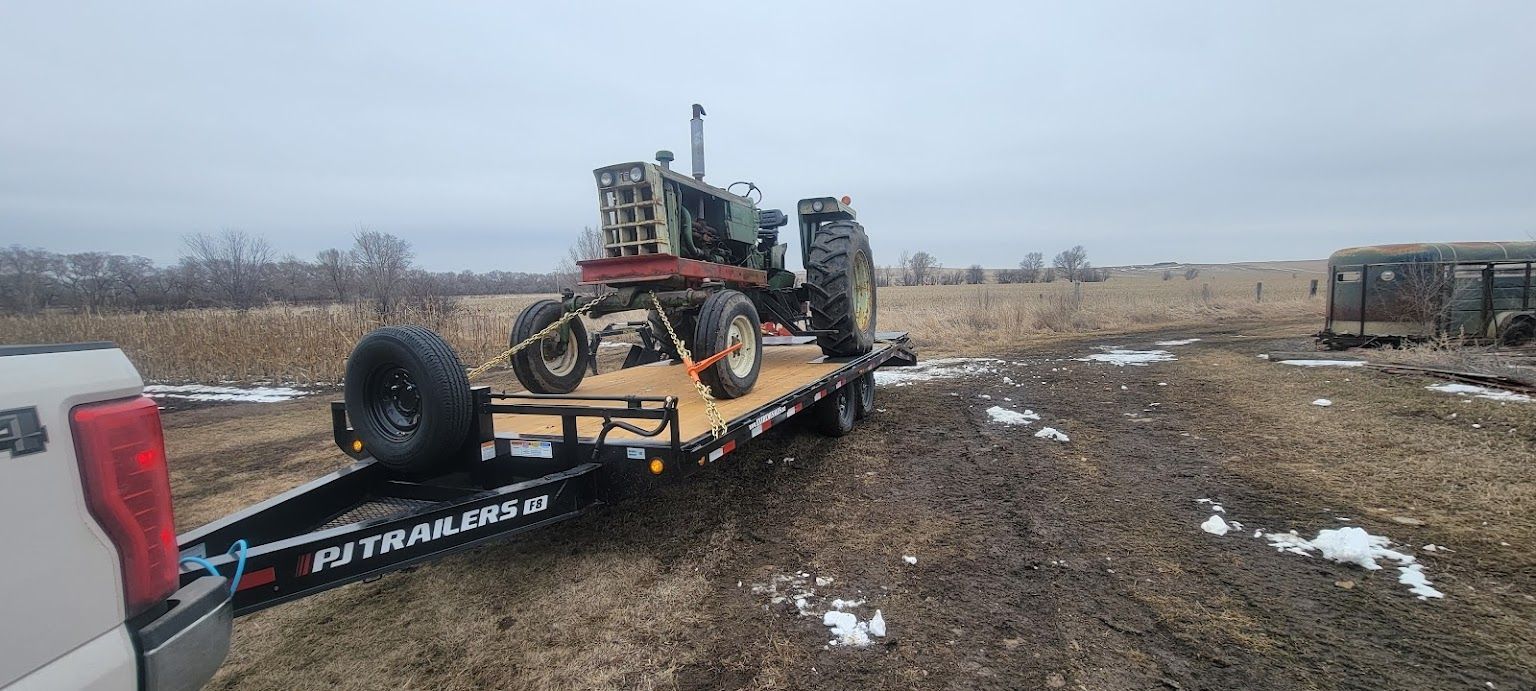 A tractor is being towed by a trailer on a dirt road.
