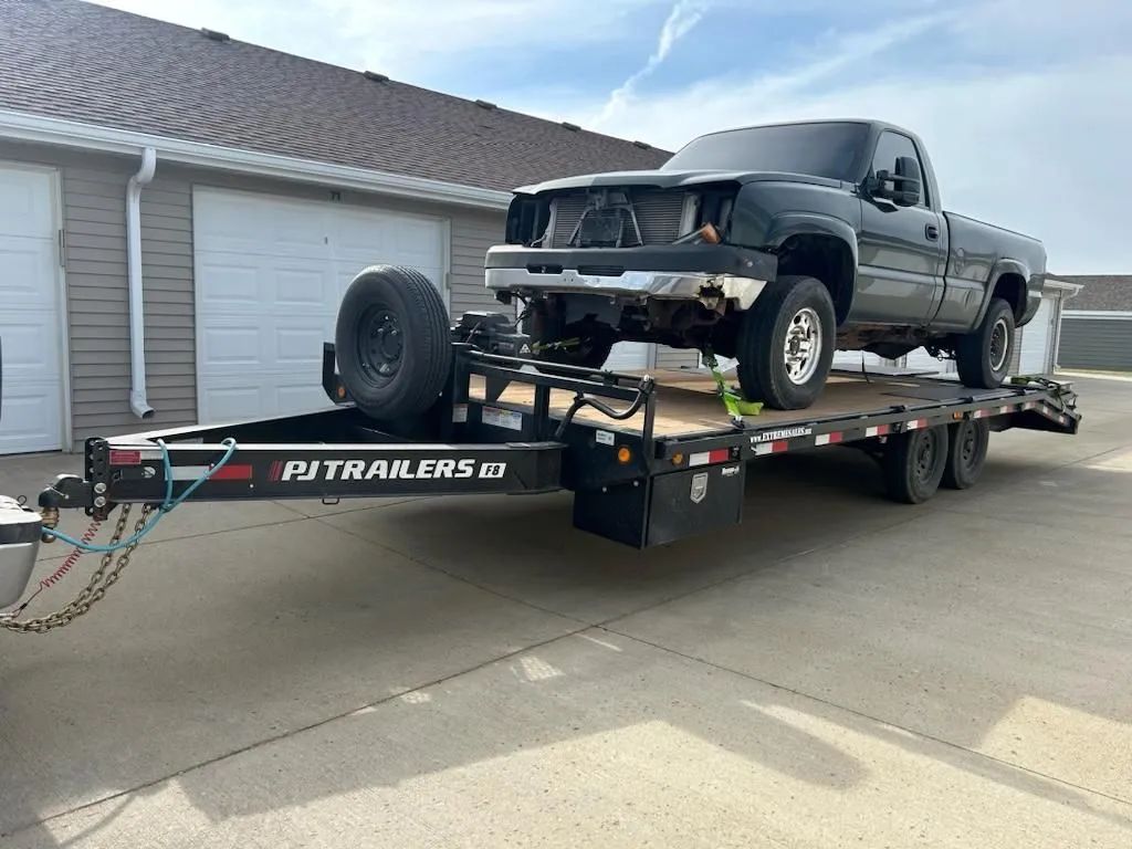 Black pickup truck on a trailer, parked on pavement near a building.