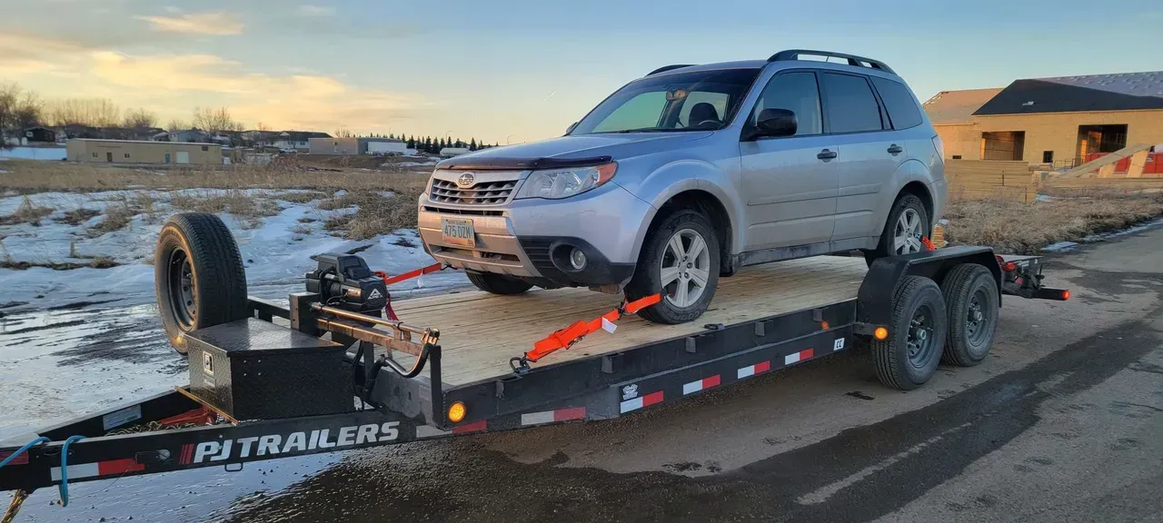 A silver suv is sitting on top of a trailer.