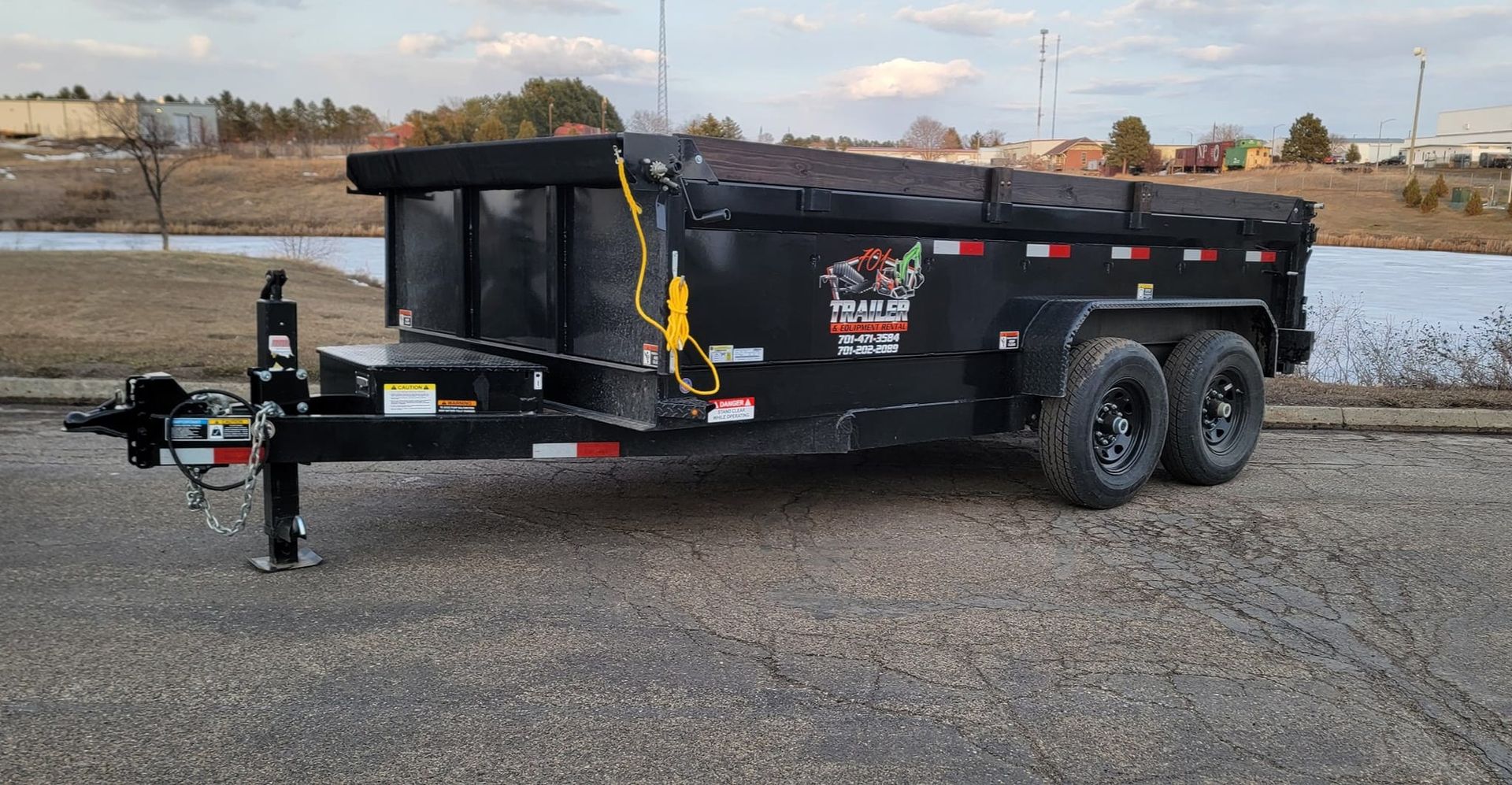 A dump trailer is parked on the side of the road next to a body of water.