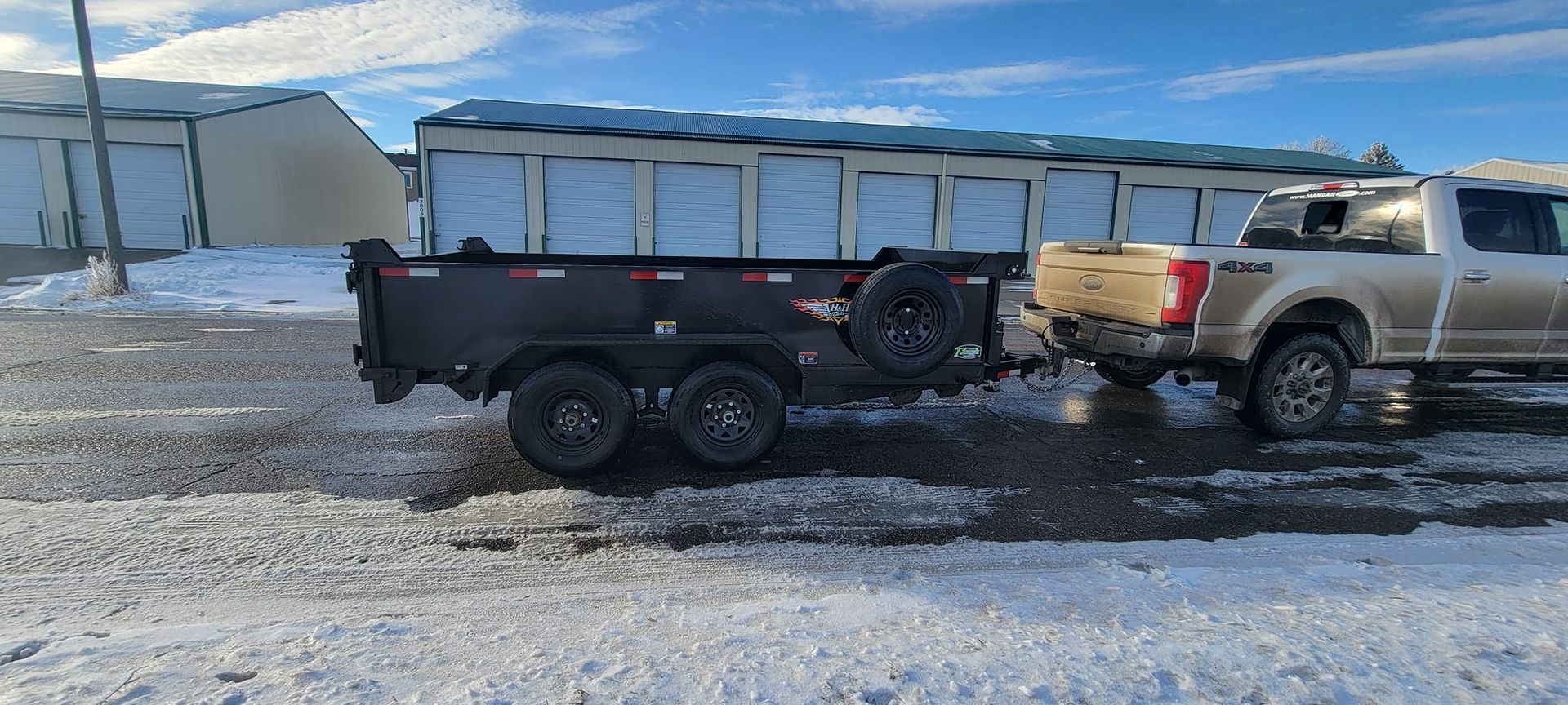 A truck is towing a dump trailer down a snowy road.