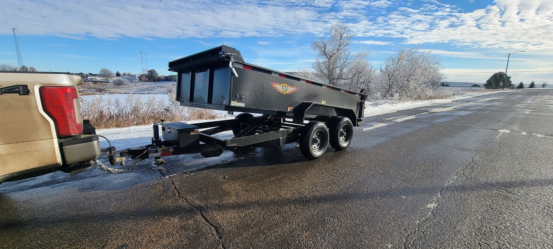 A dump truck is towing a trailer down a snowy road.