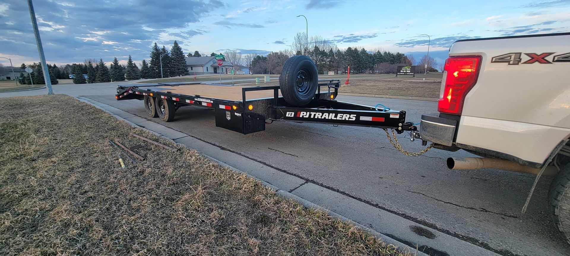 A white truck is towing a trailer down a street.