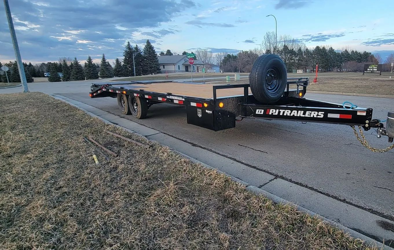 A black flatbed trailer parked on a paved road with a spare tire mounted.