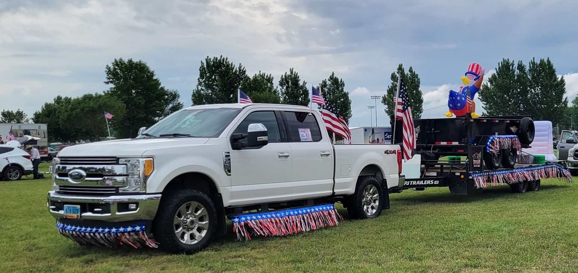 A white truck with a trailer attached to it is parked in a grassy field.