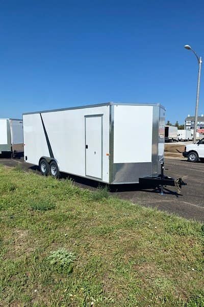 A white trailer is parked on the side of the road in a grassy field.