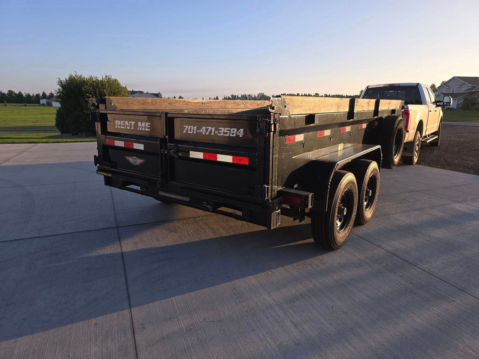 A dump trailer is parked next to a truck in a driveway.