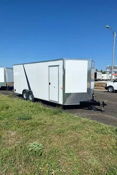 A white trailer is parked in a grassy field next to a road.