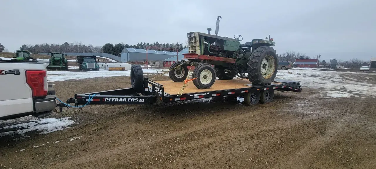 A tractor is being towed by a trailer on a dirt road.