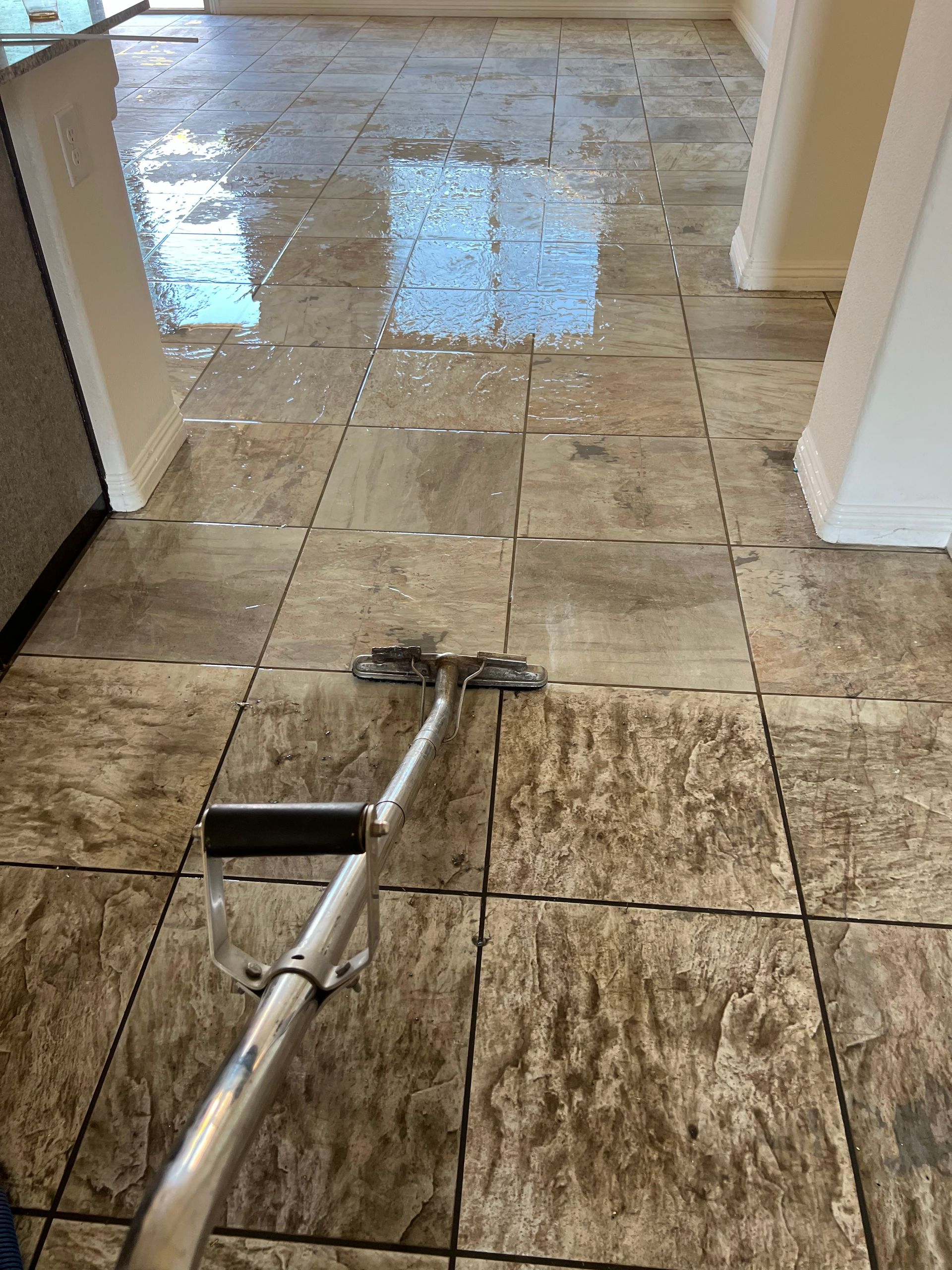 A cleaning machine is washing a dirty tile floor, leaving behind clean, wet patches.