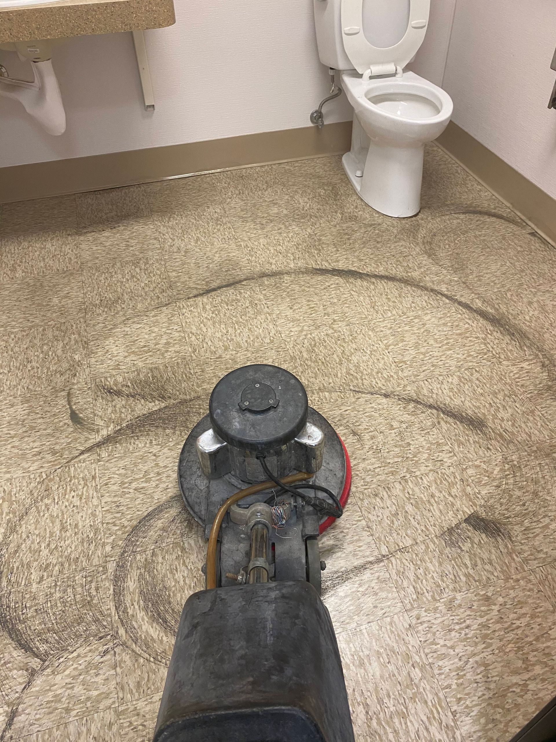 Floor scrubber cleaning a restroom floor near a toilet.