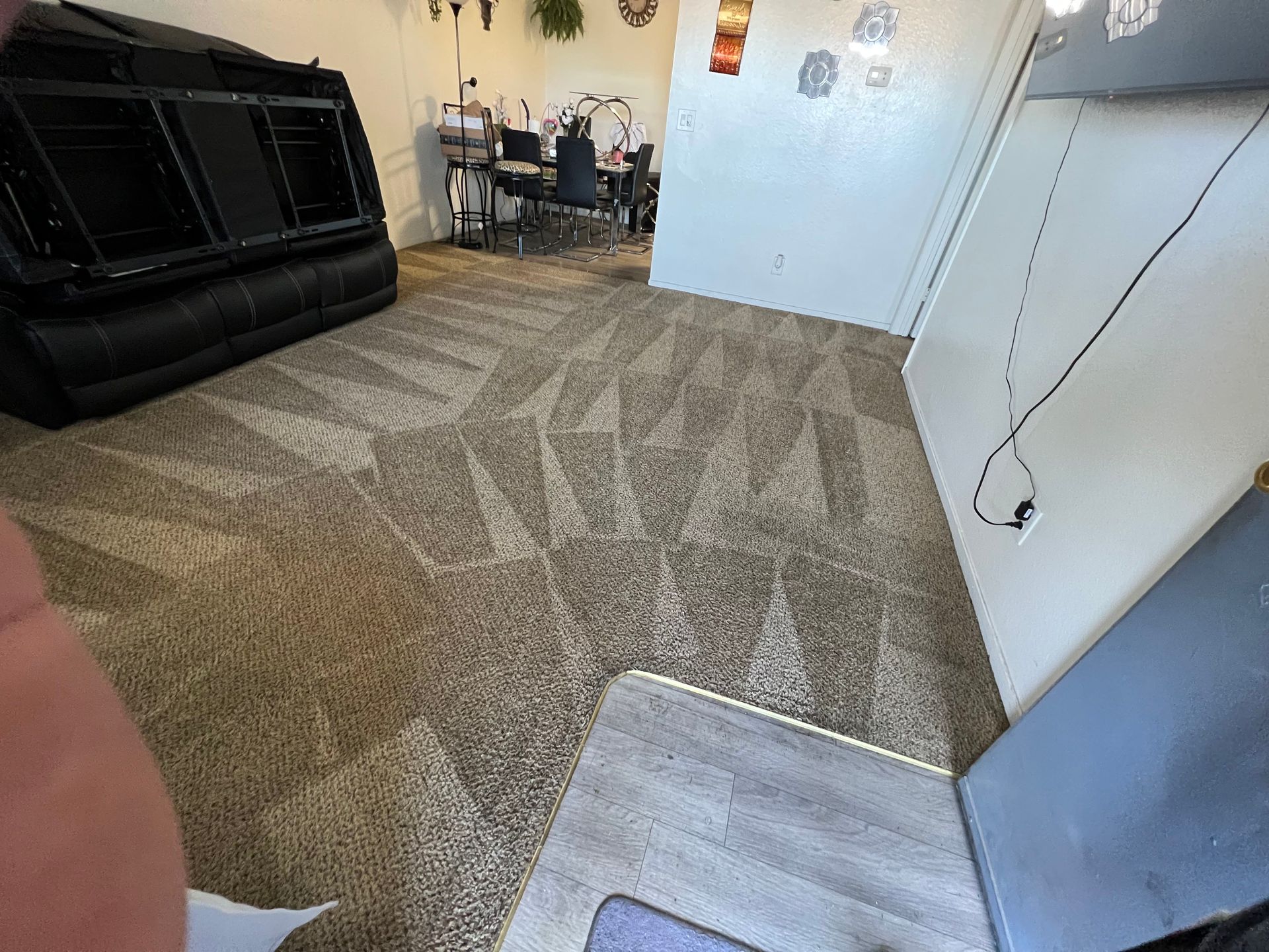 Room with patterned carpet, black sofa, and an open doorway leading to a dining area.