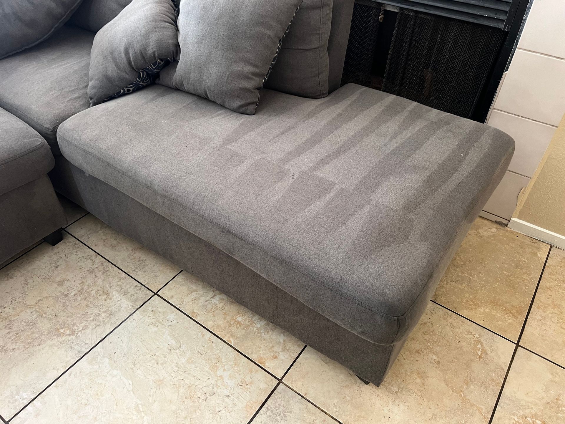 Gray sectional sofa with visible cleaning marks on the ottoman, set on tiled floor.