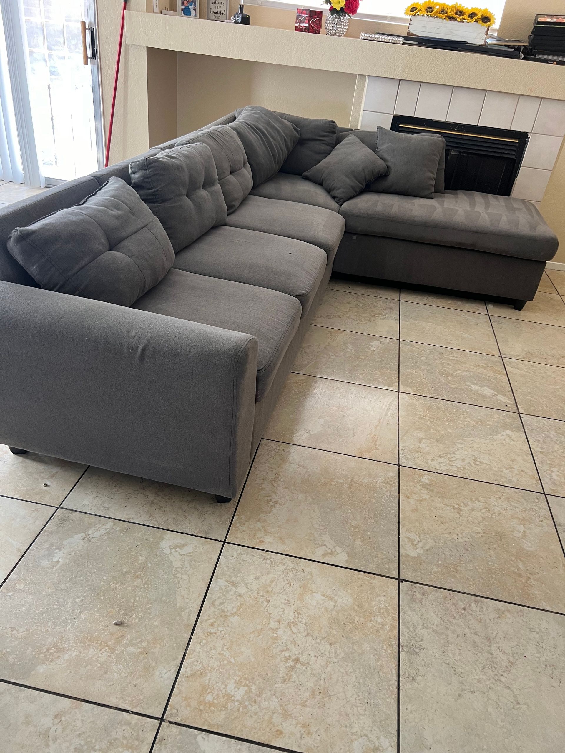 Gray sectional sofa in a living room with tile flooring and a fireplace.