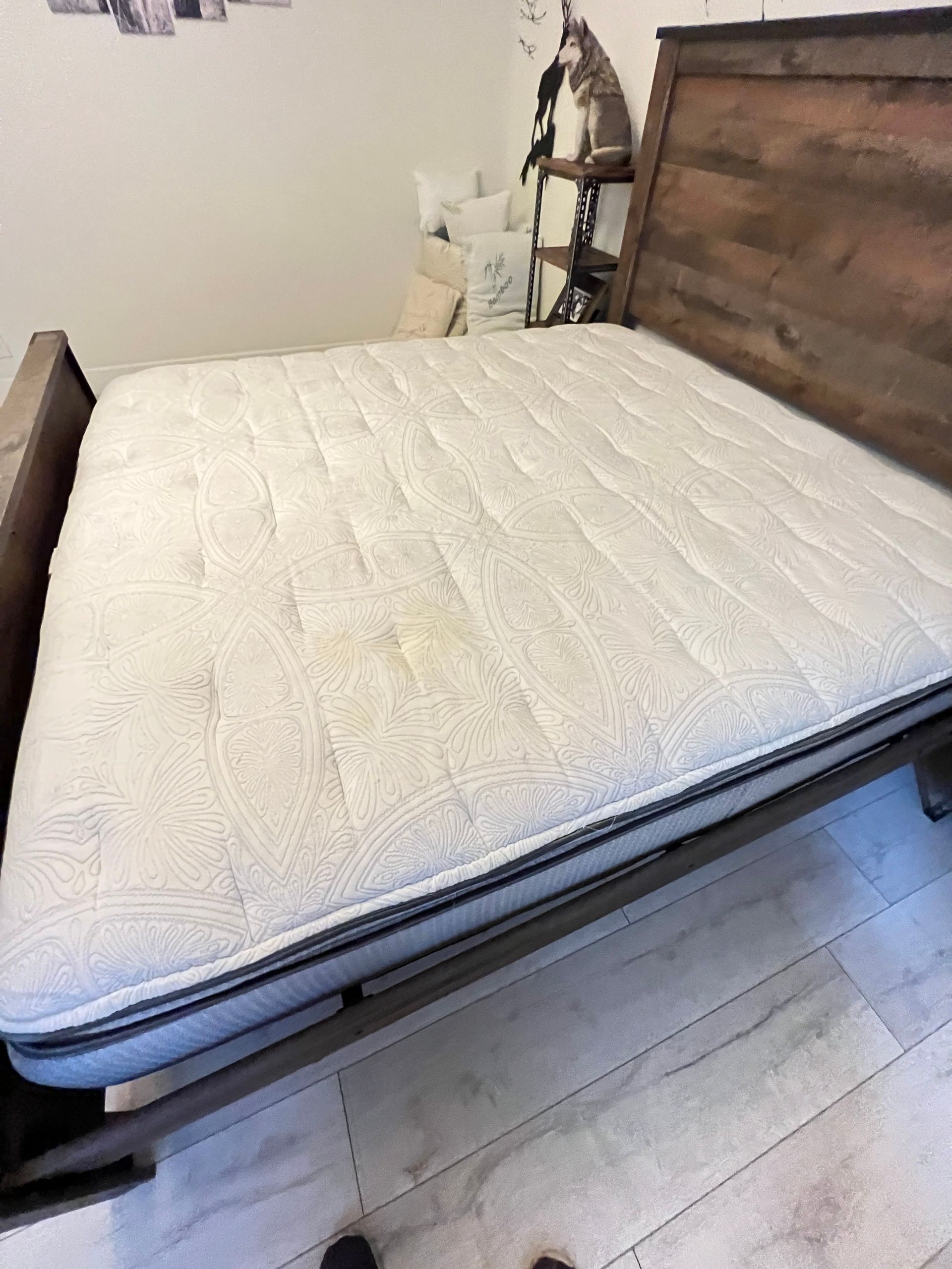 Bed with a wooden headboard and a mattress with stains on a light-colored floor.