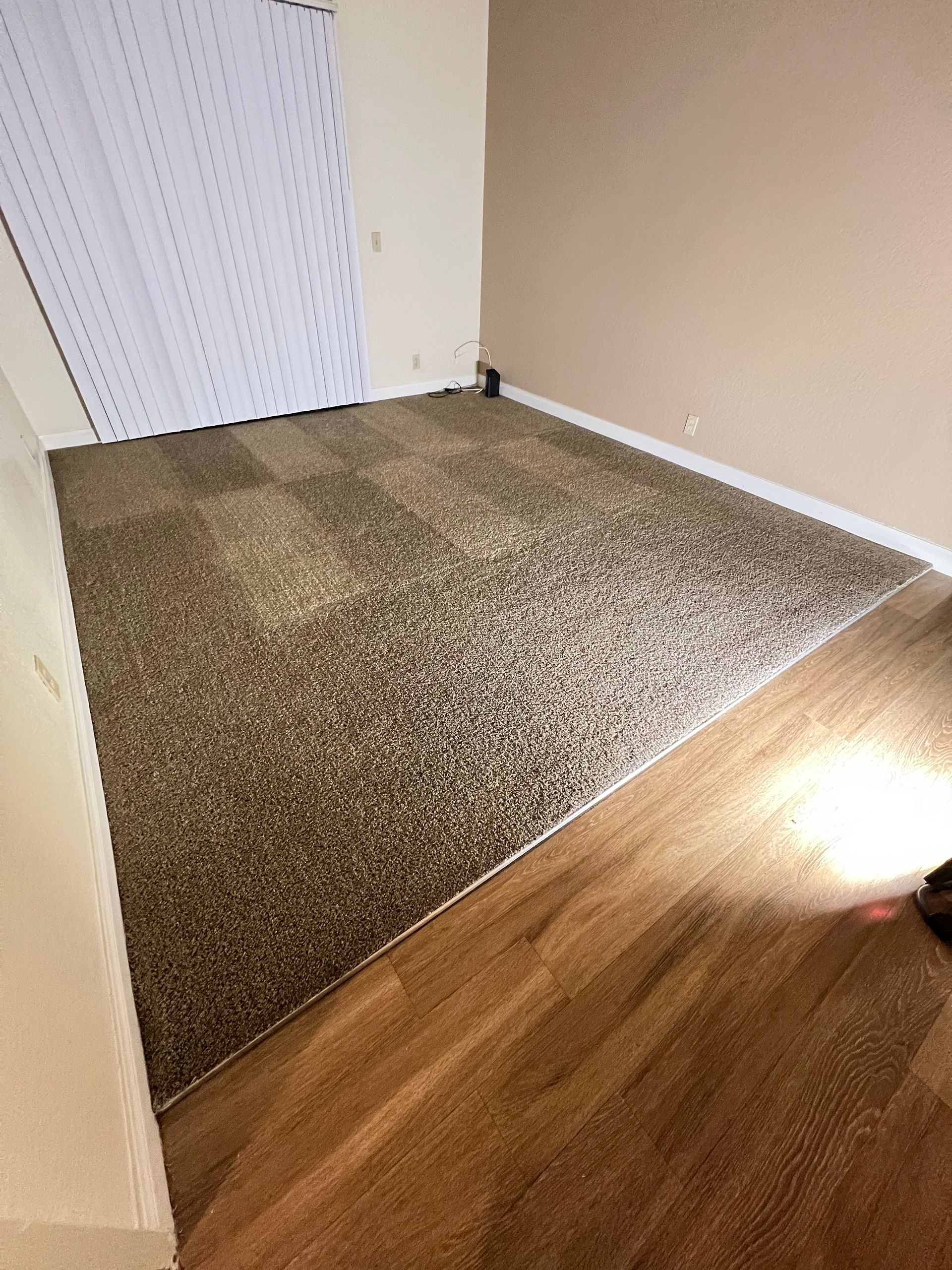 Brown and tan carpet and wood flooring in a room with tan walls and white closet doors.