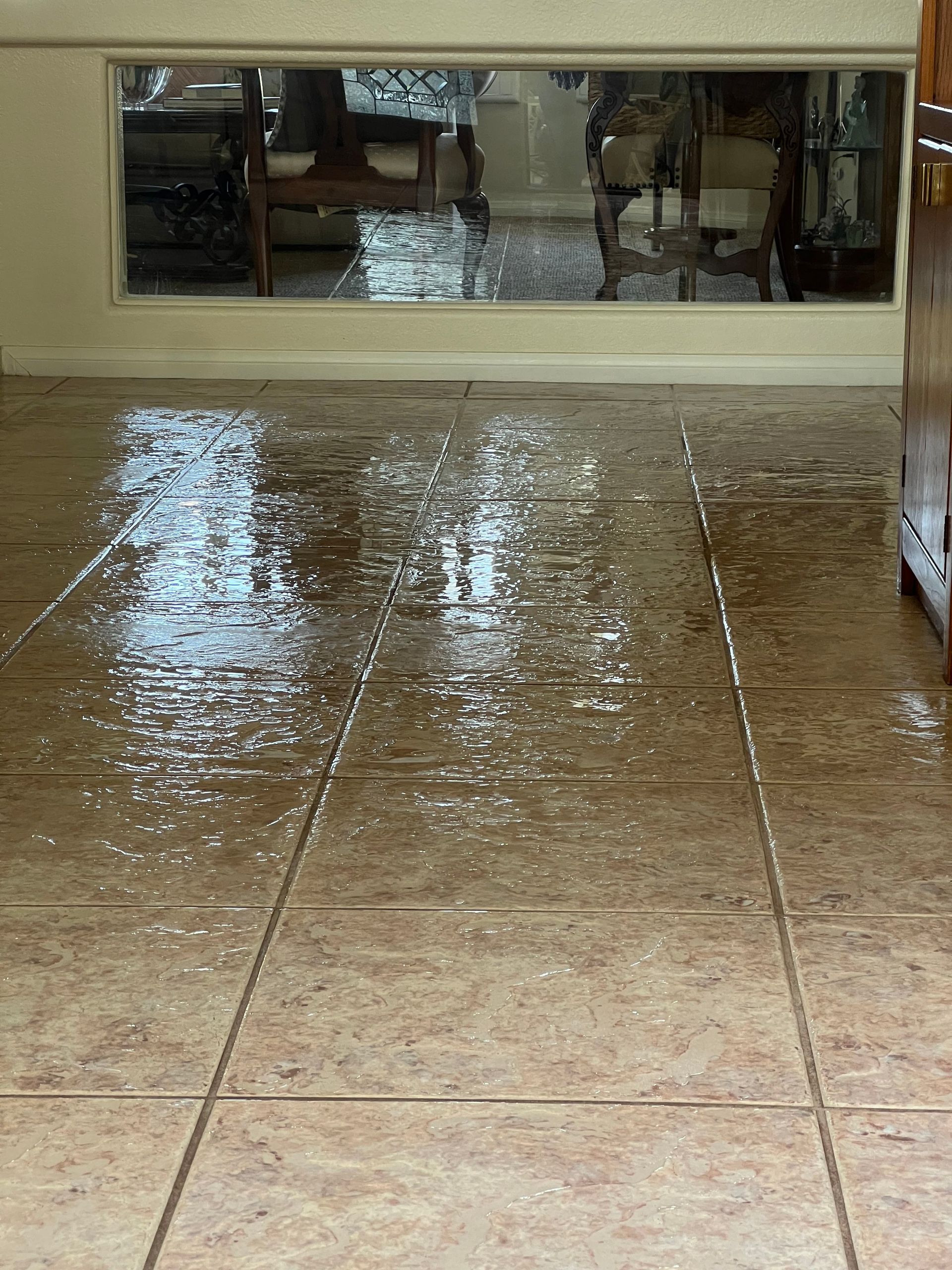 Wet tiled floor in front of a window, reflecting light and objects in the room.