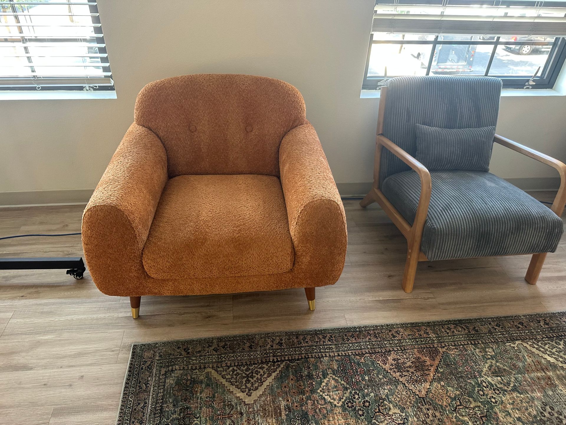 Two armchairs on a rug near a window. One is orange, textured, and rounded; the other is blue patterned with a wooden frame.