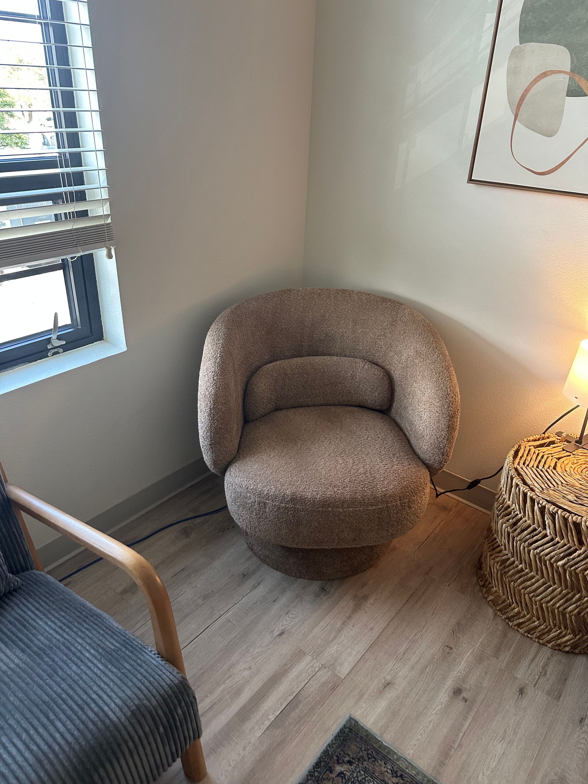 Cozy boucle chair in a corner next to a window with blinds.