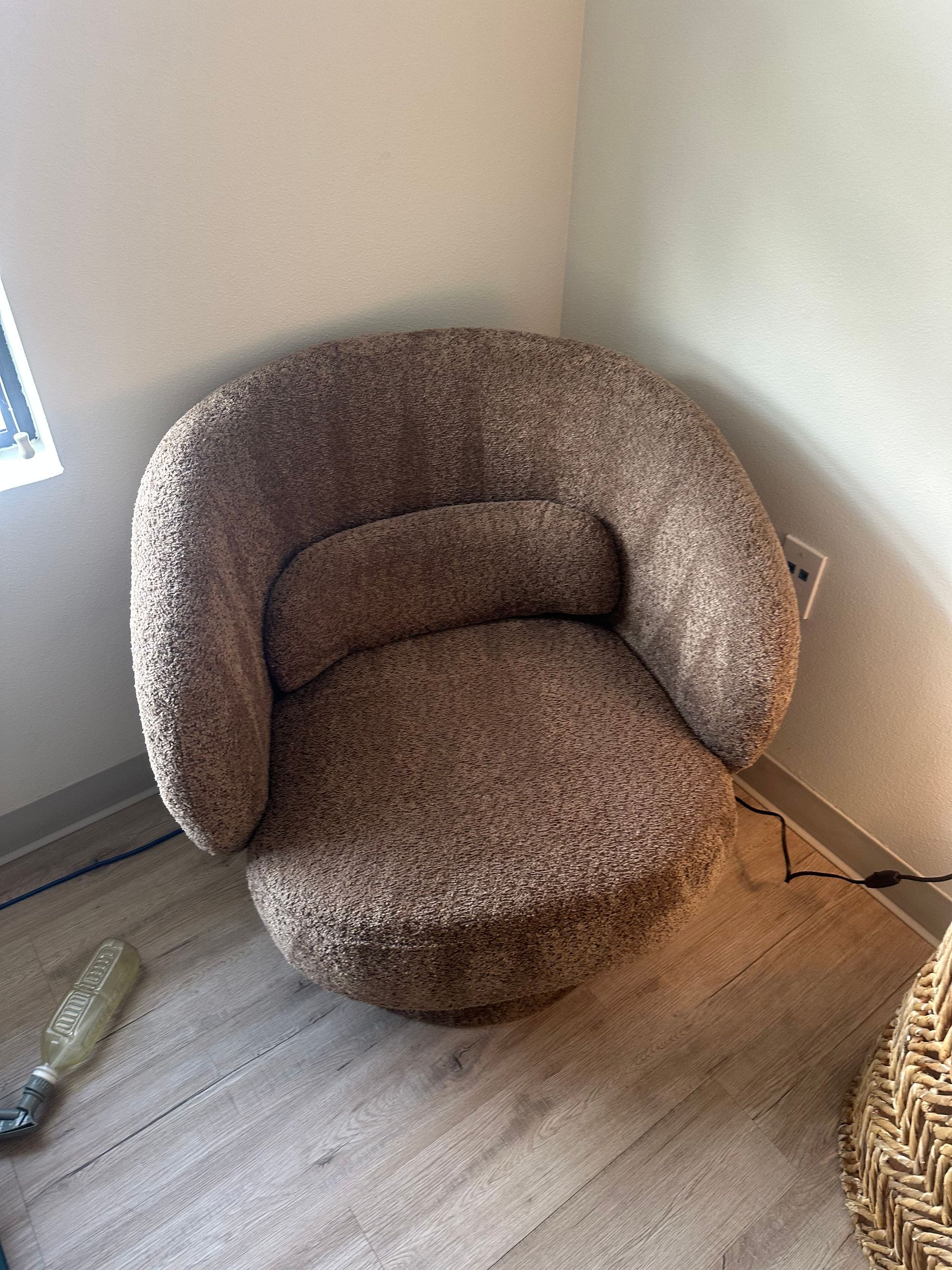 Brown, round armchair with a textured fabric. It sits in the corner of a room, next to a beige rug.