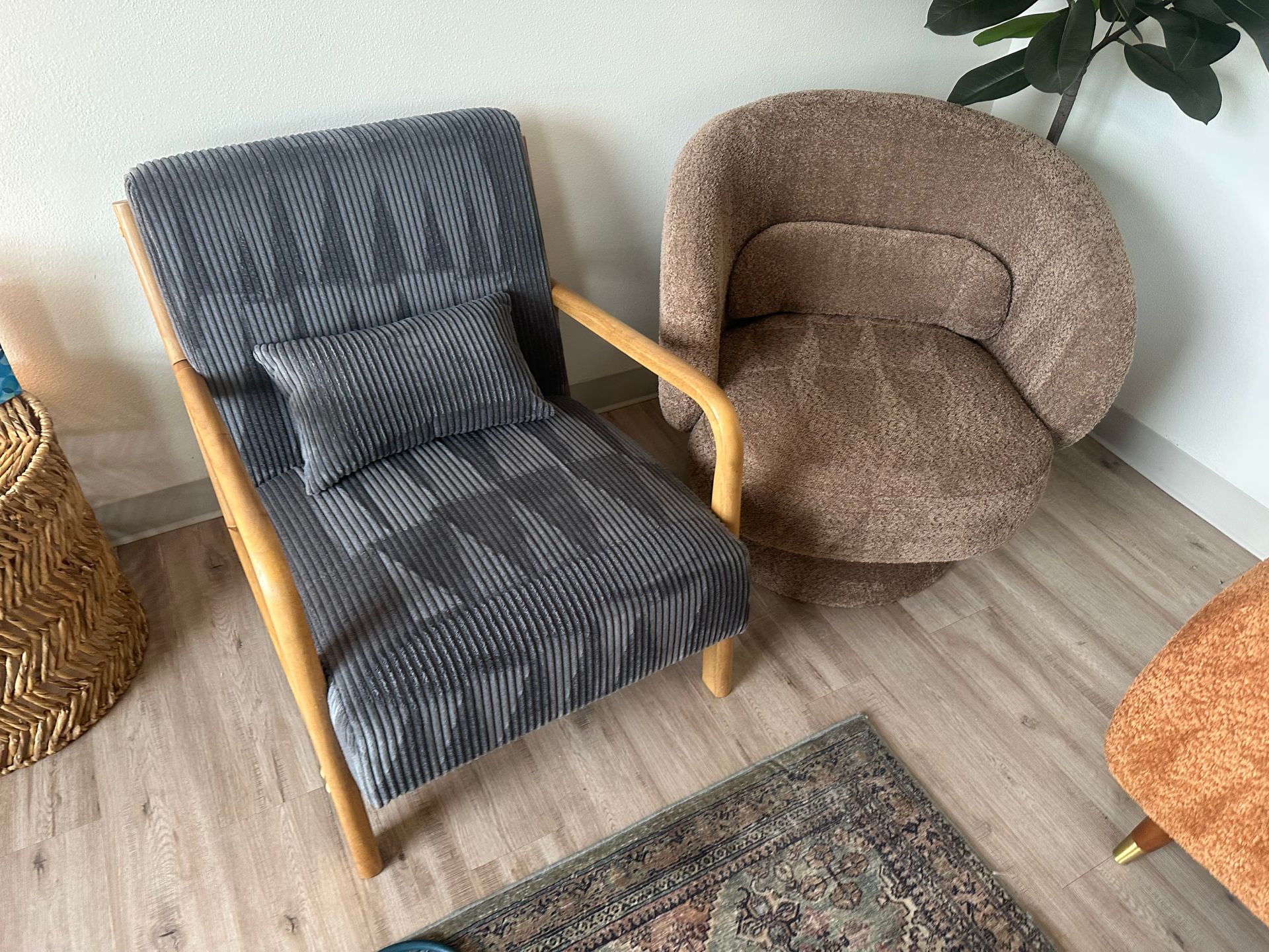 Two armchairs, one grey ribbed, one brown, wood frames, rug on light wood floor.