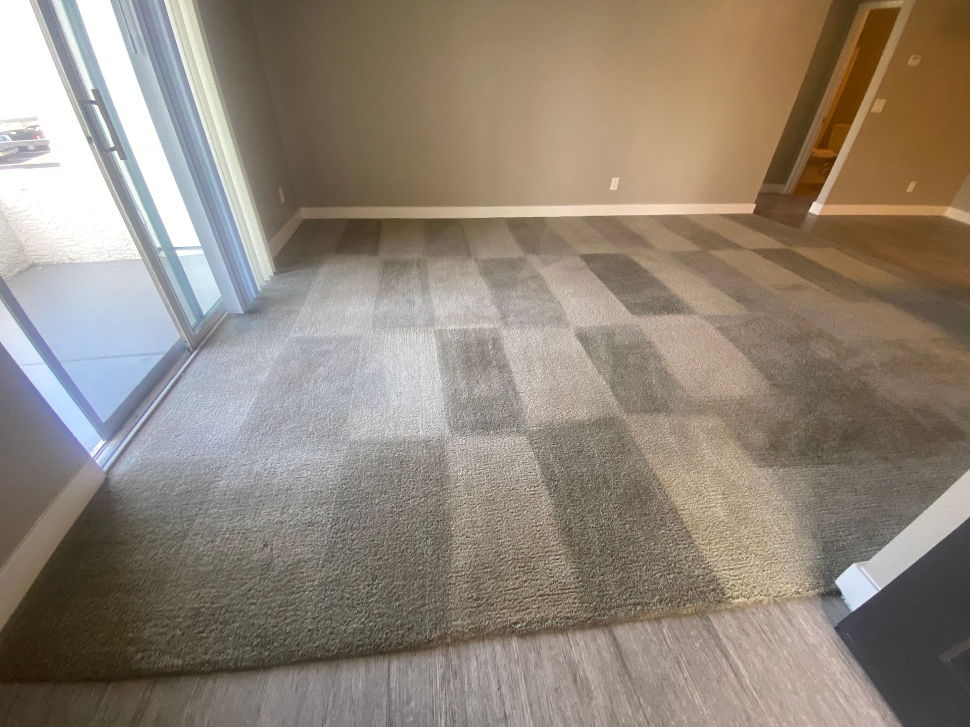 A room with a checkered pattern carpet. Sliding door to a balcony on the left.