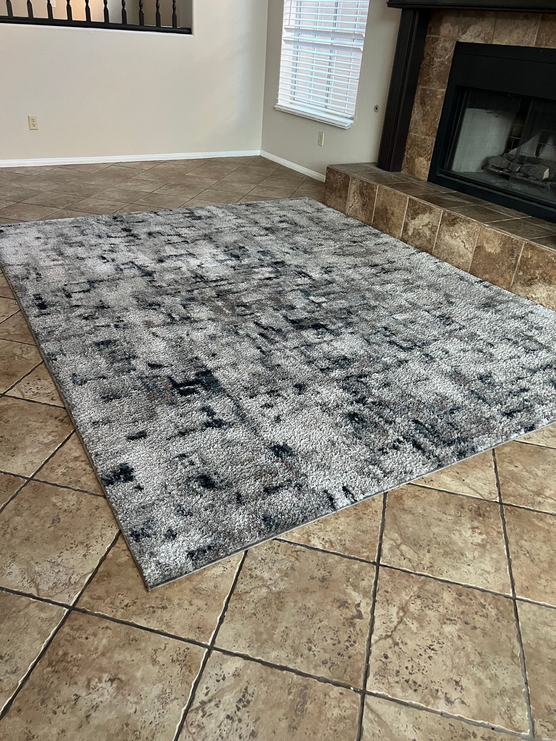Shaggy gray rug on a tiled floor in front of a fireplace.