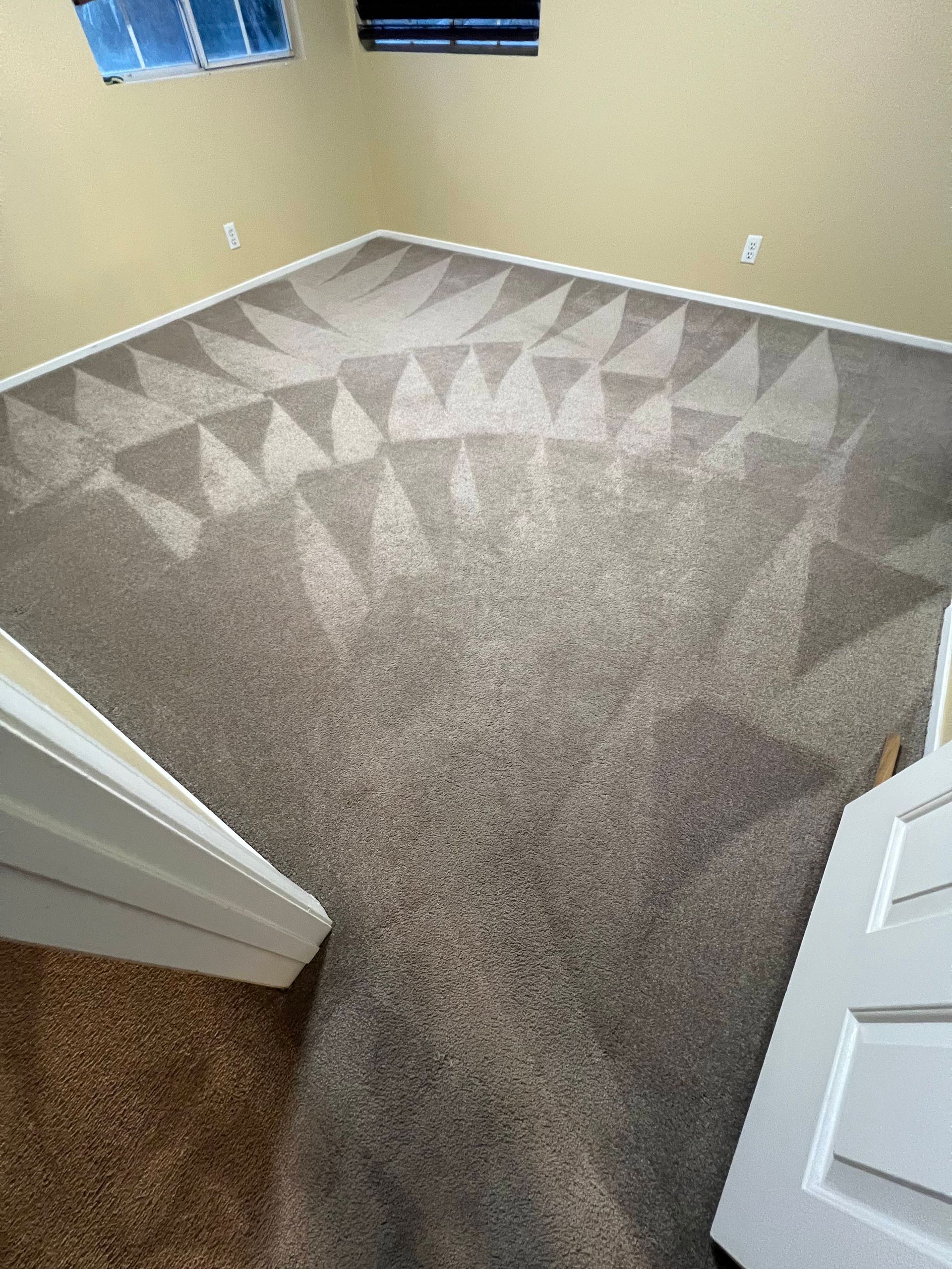 A room with patterned carpet and doorway. Beige walls and a window are also visible.