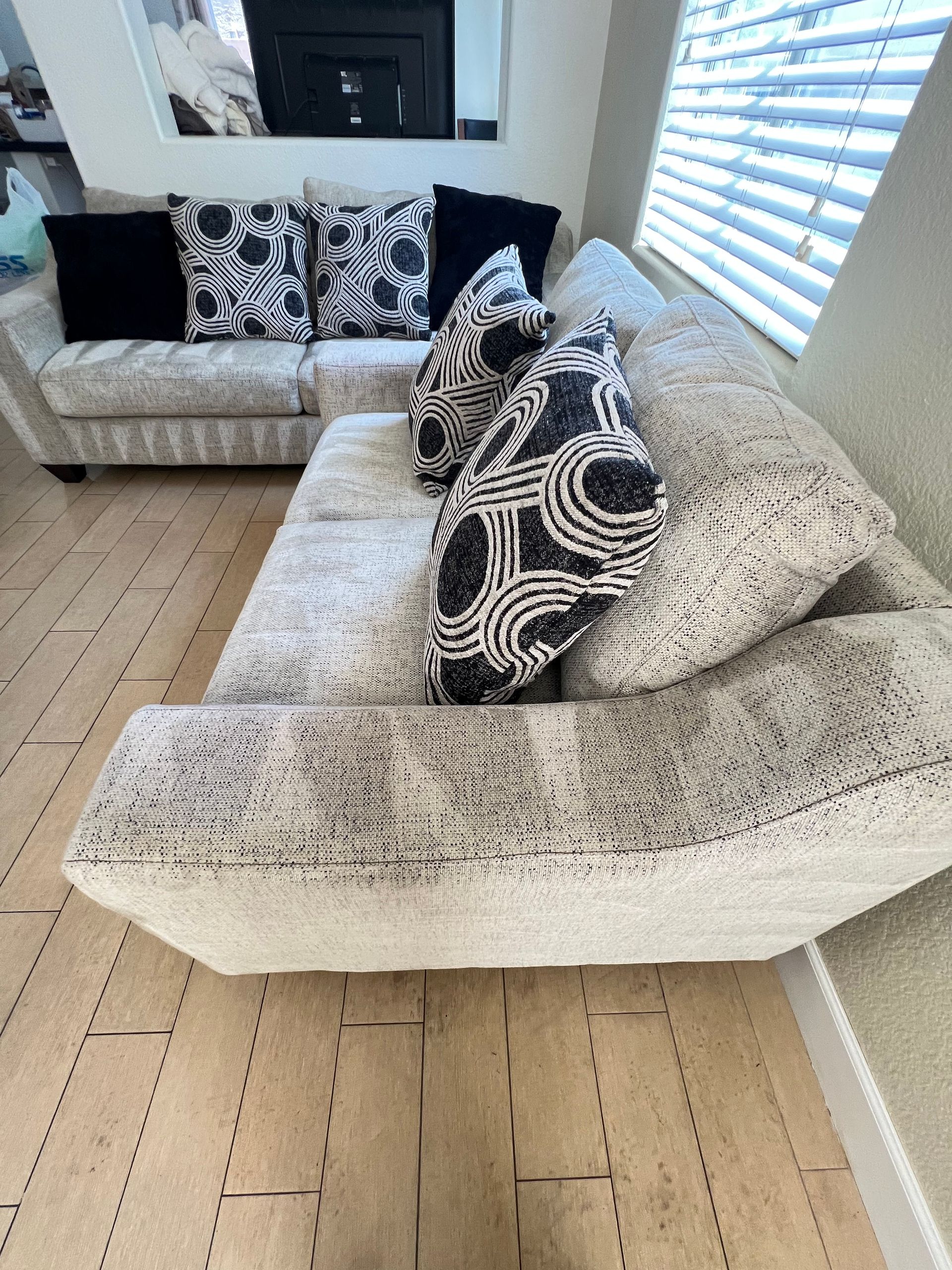 Beige sectional sofa with patterned pillows in a living room with wooden floors.