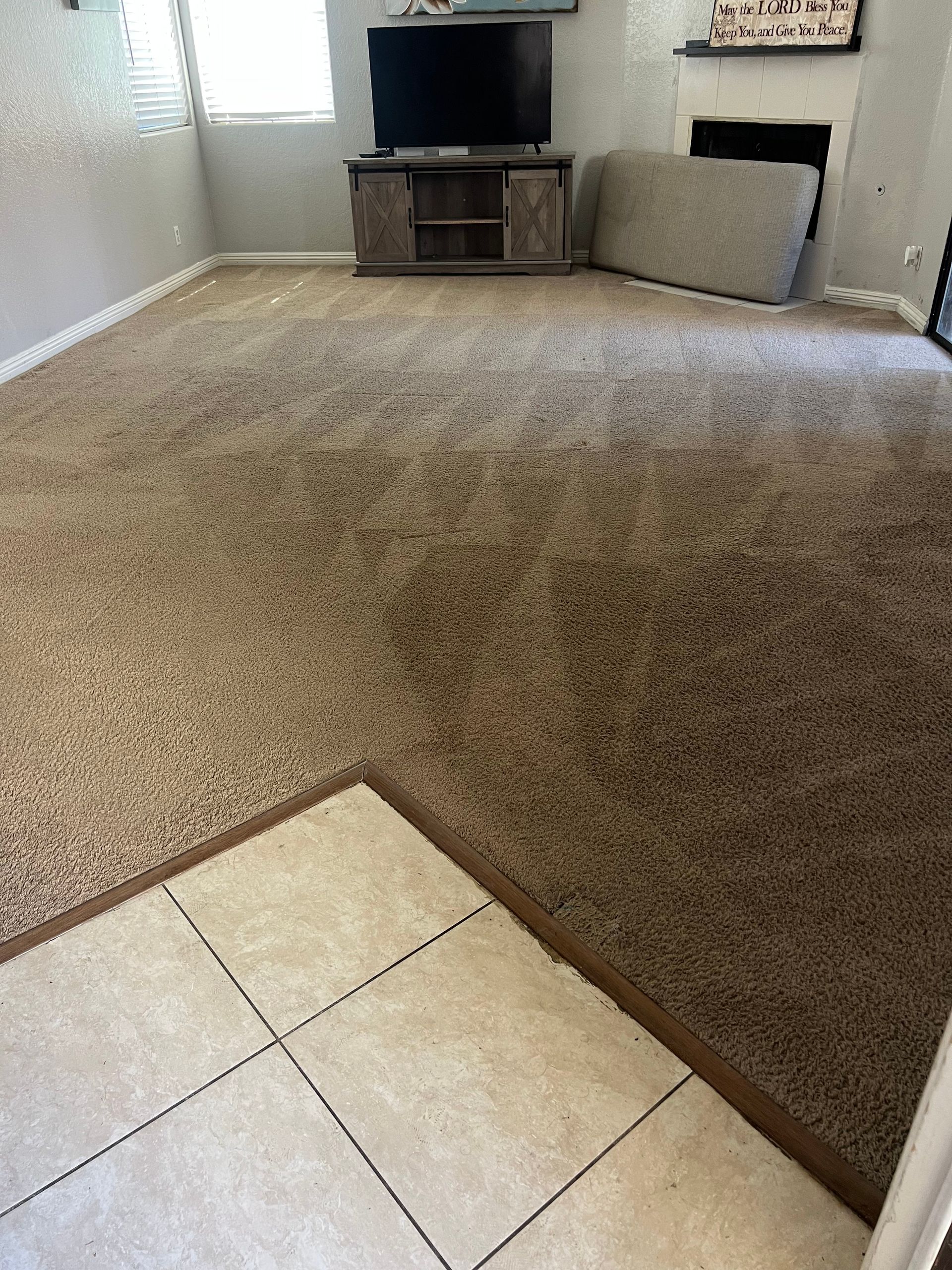 A carpeted living room with a TV, fireplace, and tile floor border.
