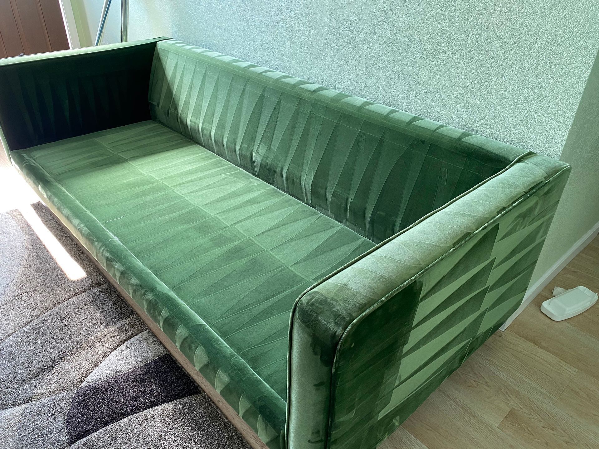 Green velvet sofa against a textured wall, with a patterned rug visible.