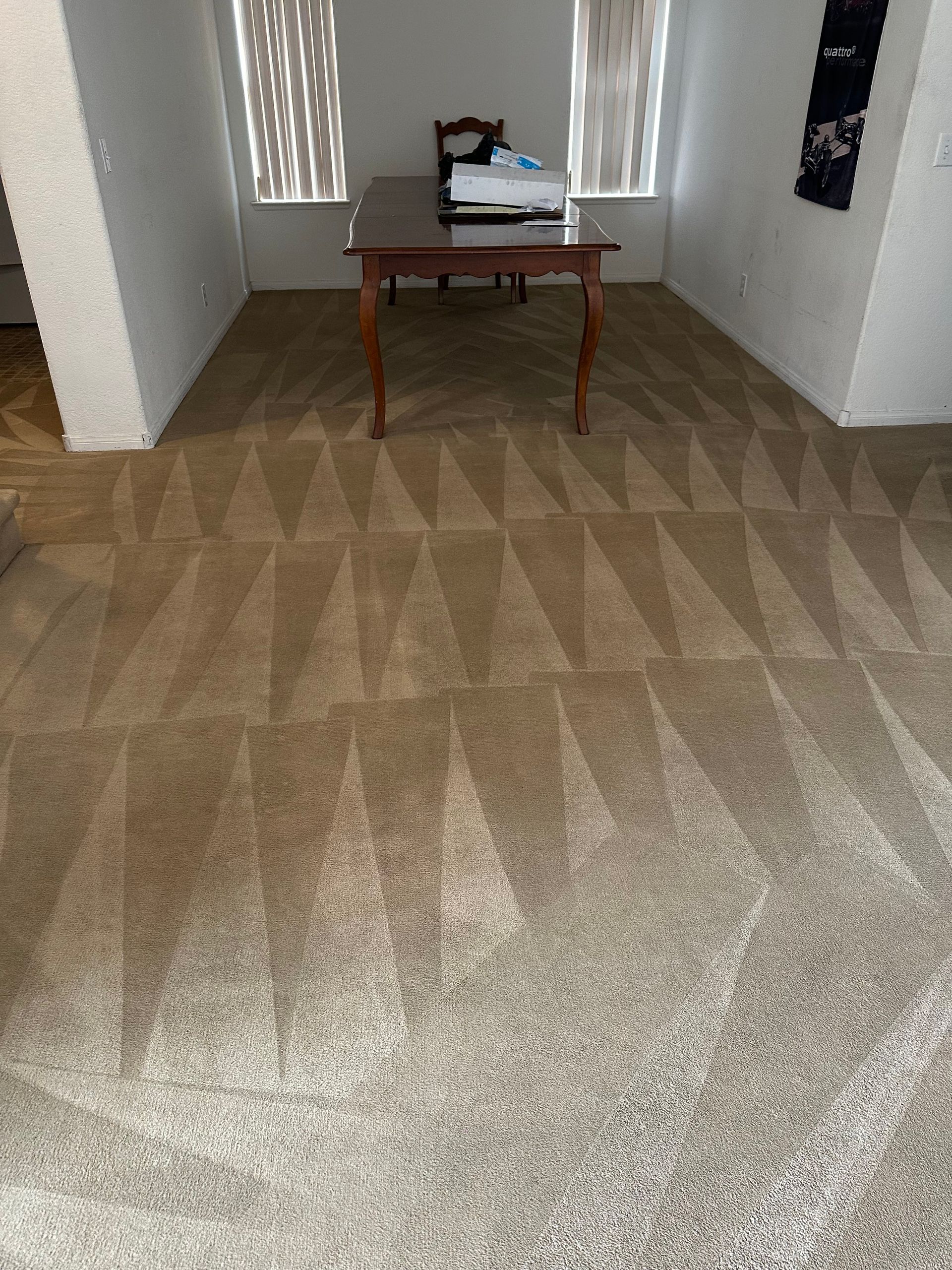 Beige carpet with geometric pattern, table with items, near windows, in room.