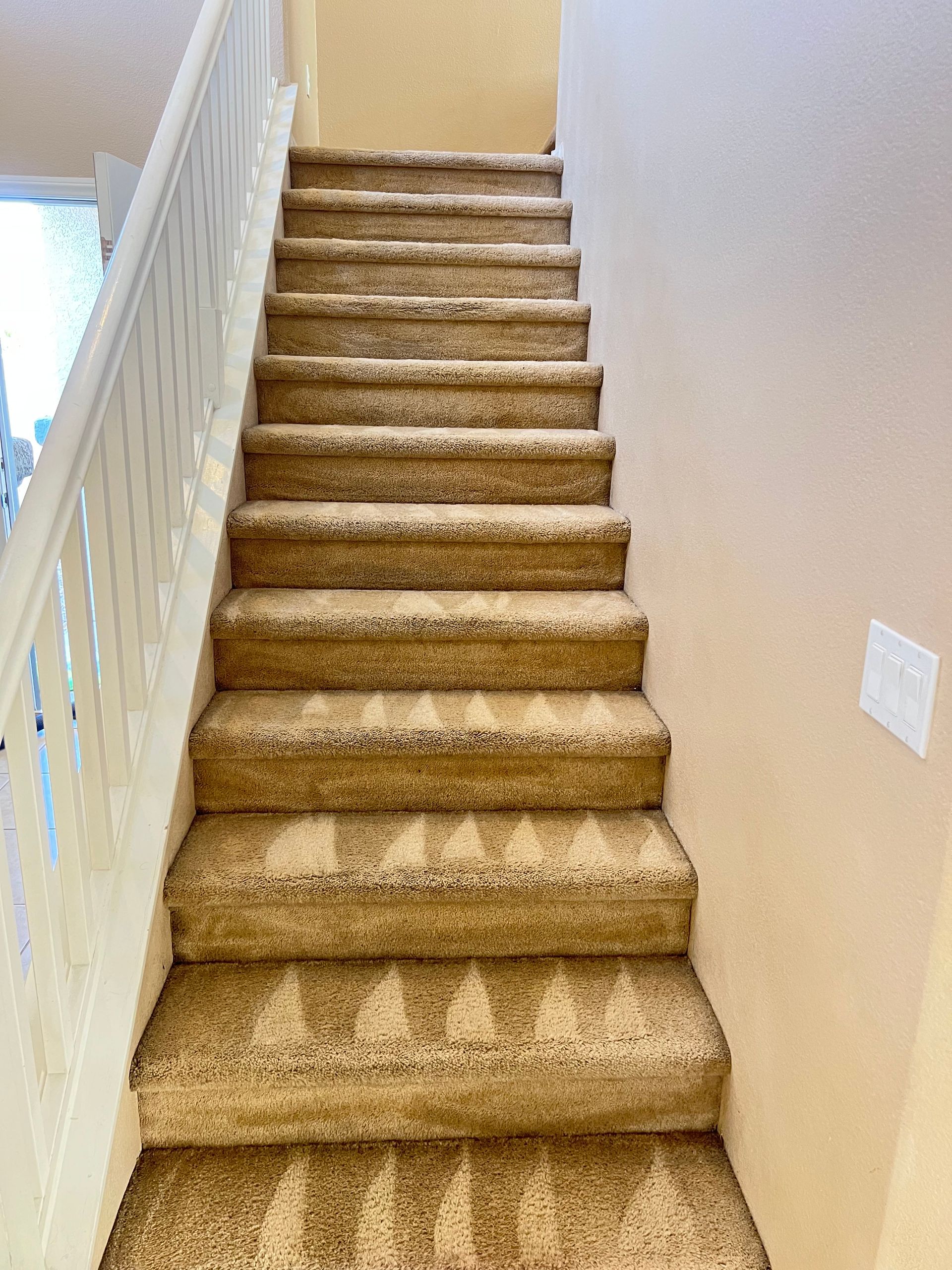 Carpeted staircase with white banister against a tan wall, leading upwards.