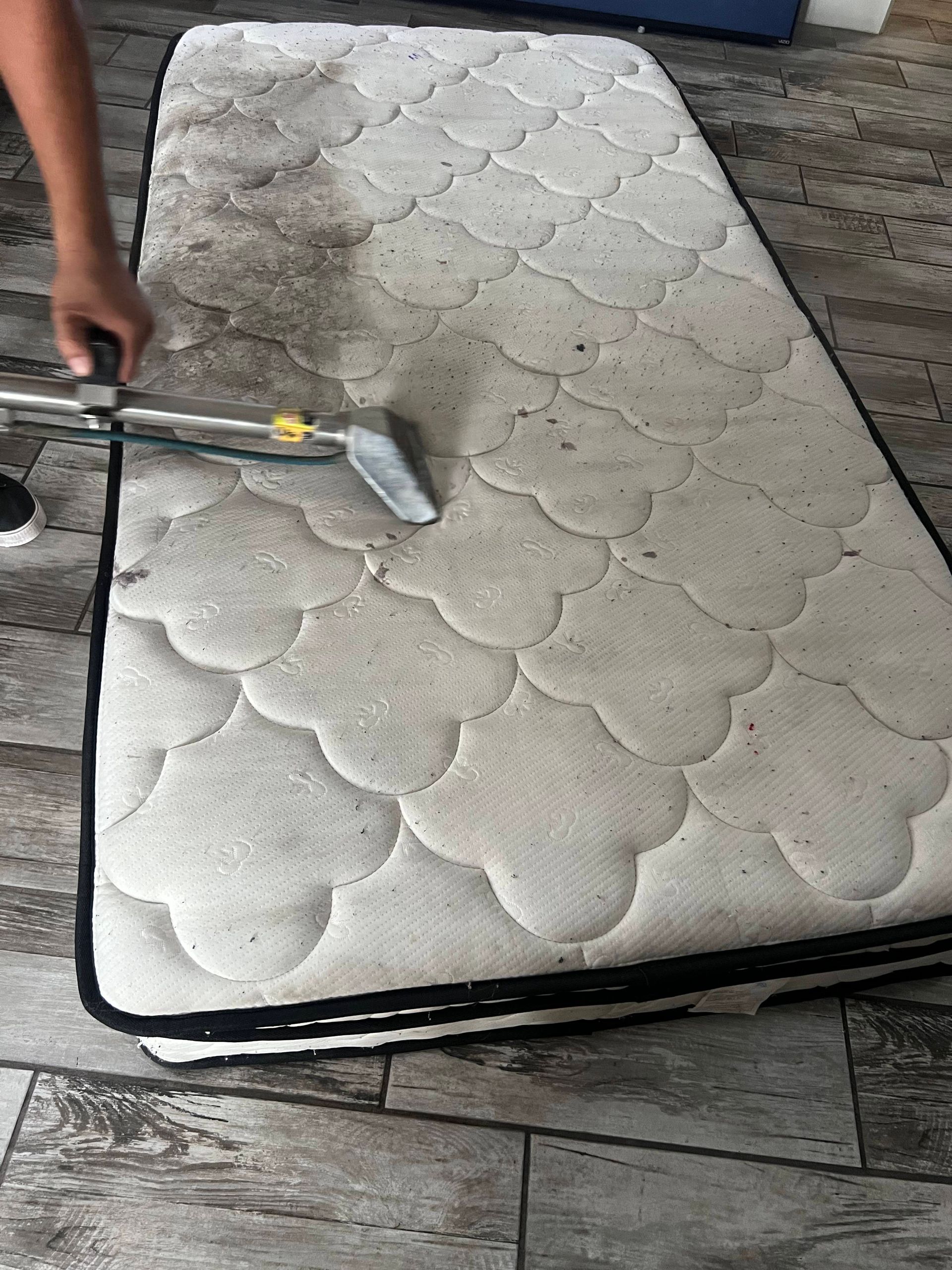 A person cleaning a dirty mattress with a handheld cleaning tool.