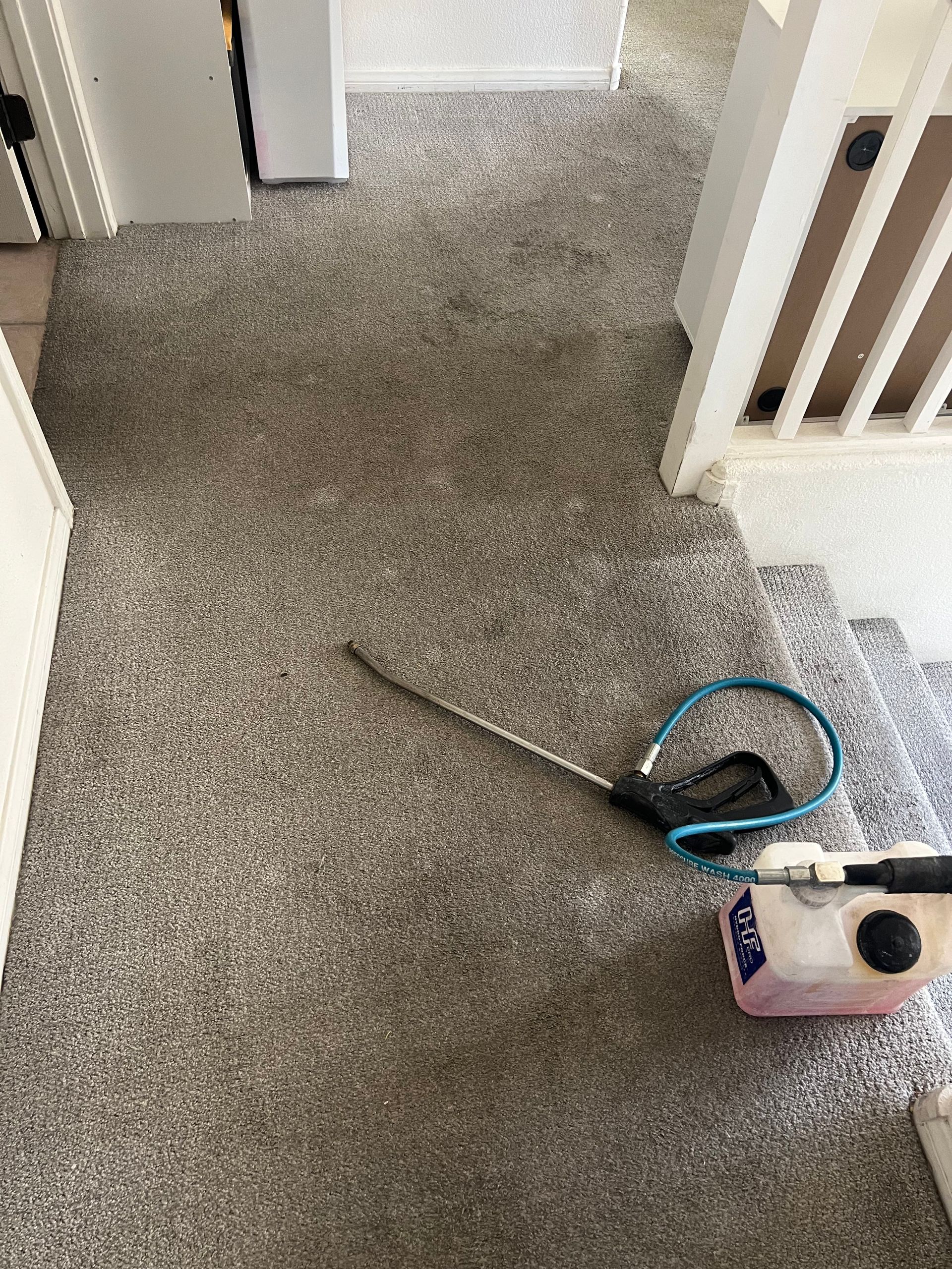 Carpet being cleaned with a spray wand and solution tank on a staircase landing.