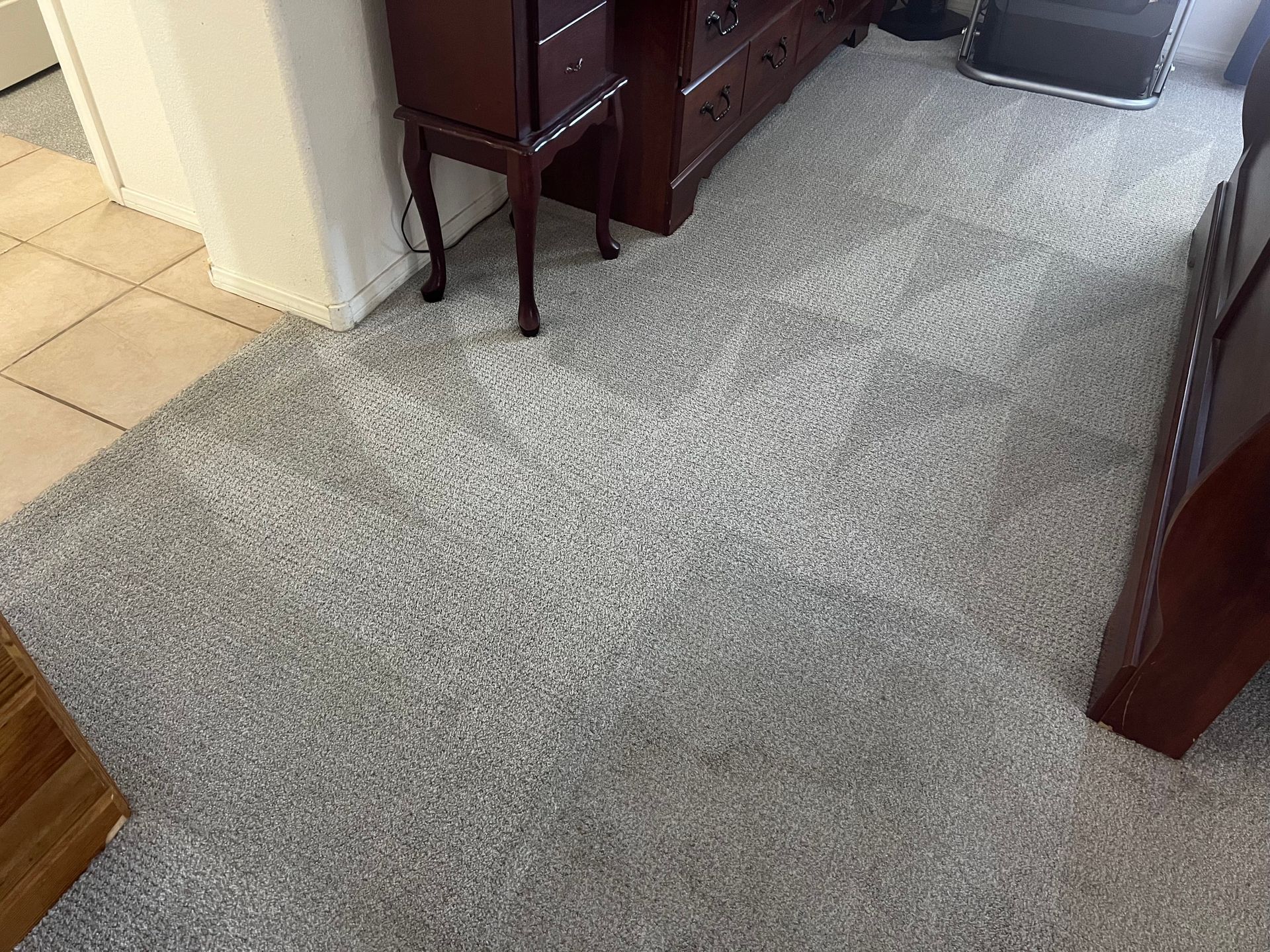 Gray carpeted floor in a room, with a dark wooden cabinet, and a door opening to tiled flooring.