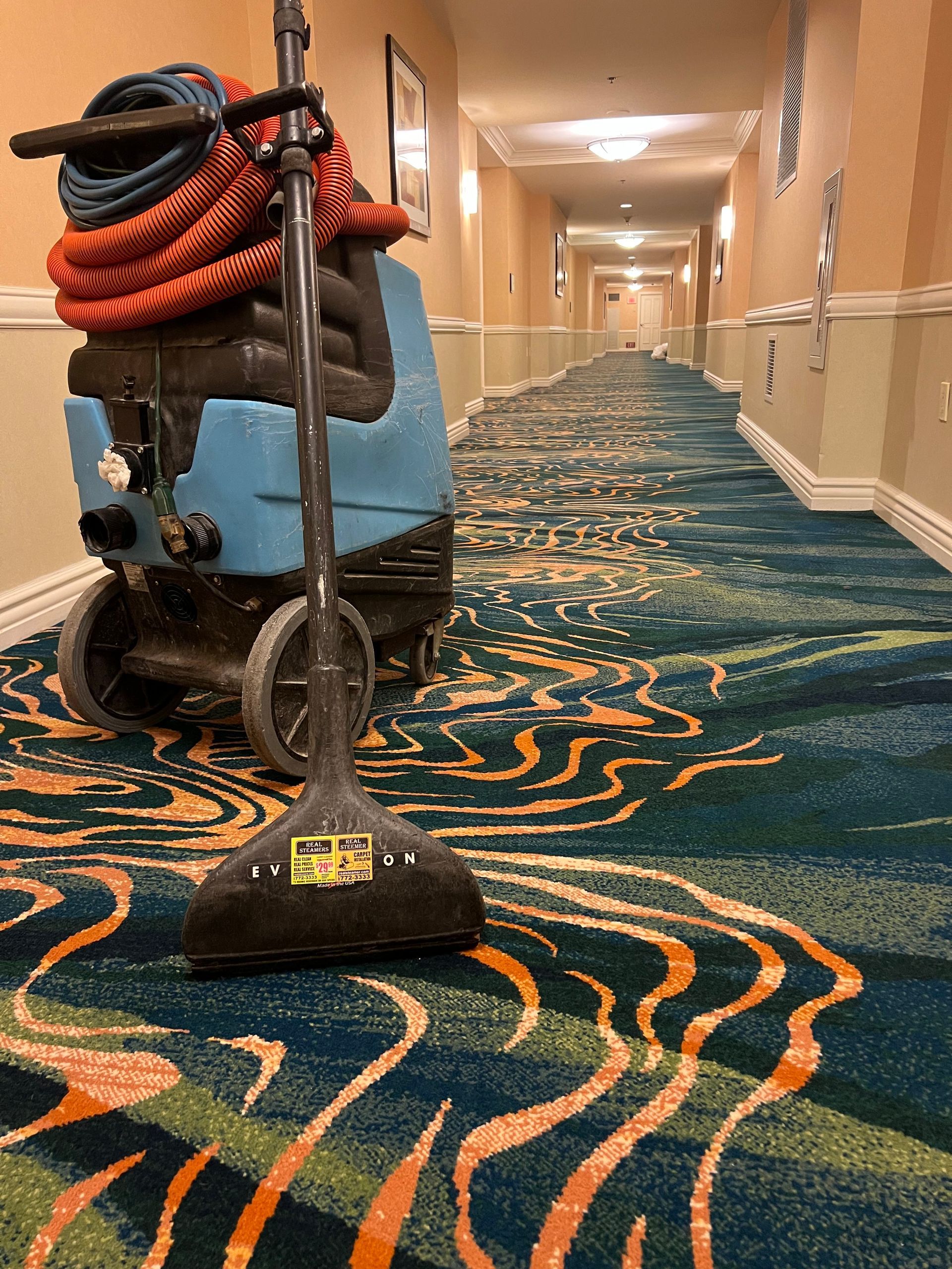 A carpet cleaning machine in a hotel hallway. The carpet is patterned with teal and orange waves.